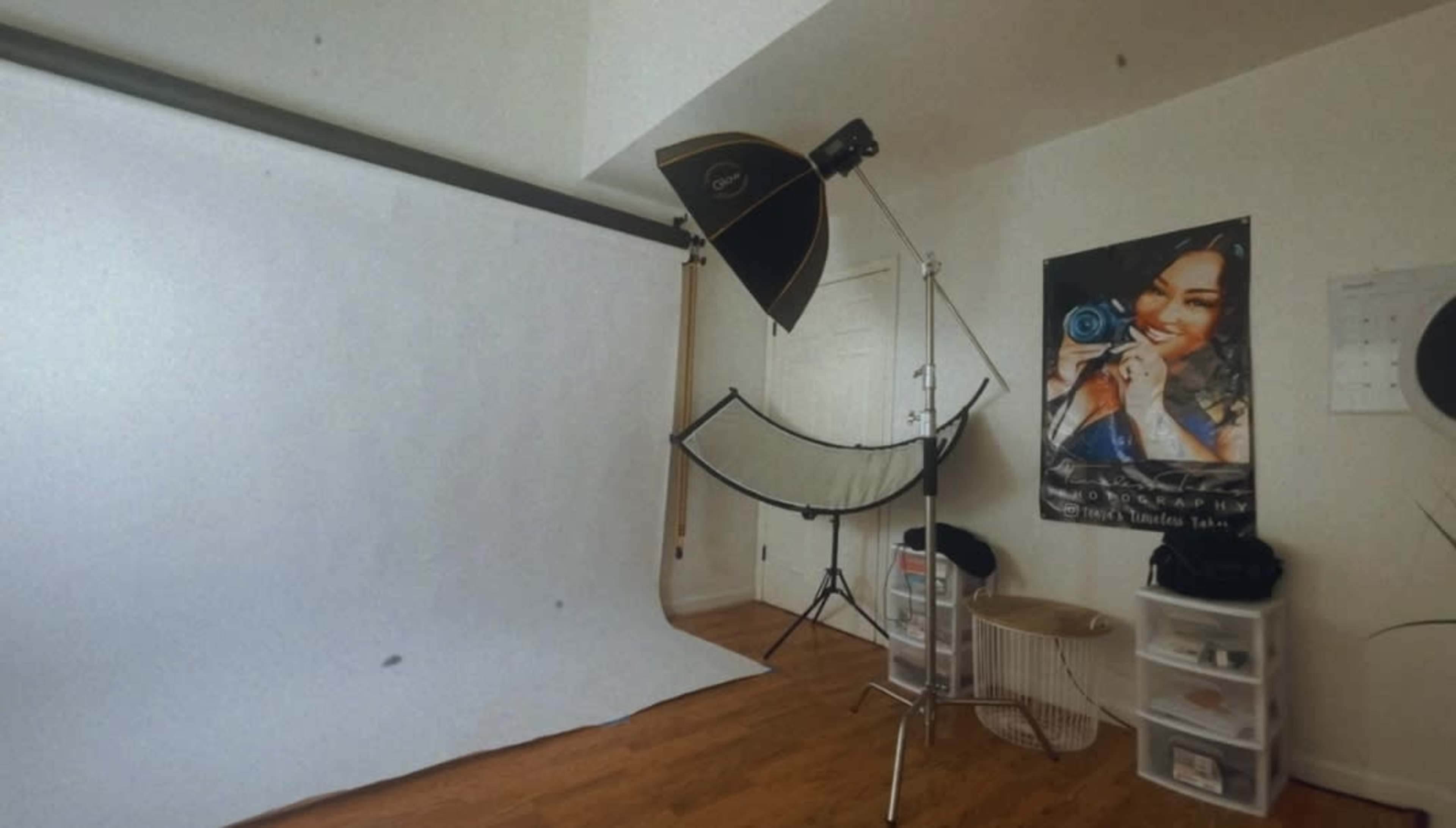 A photography studio setup with a white backdrop, lighting equipment, and a poster on the wall.