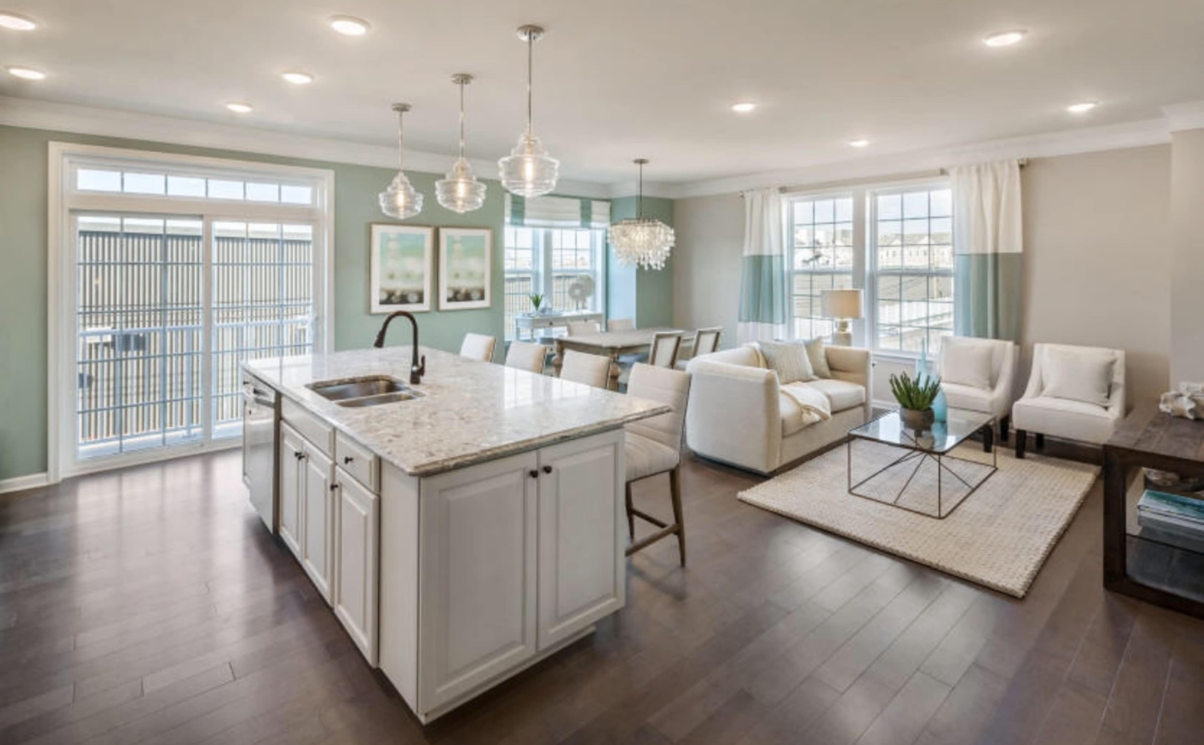 A modern open-concept living space featuring a kitchen island, dining area, and a seating area with large windows allowing natural light.