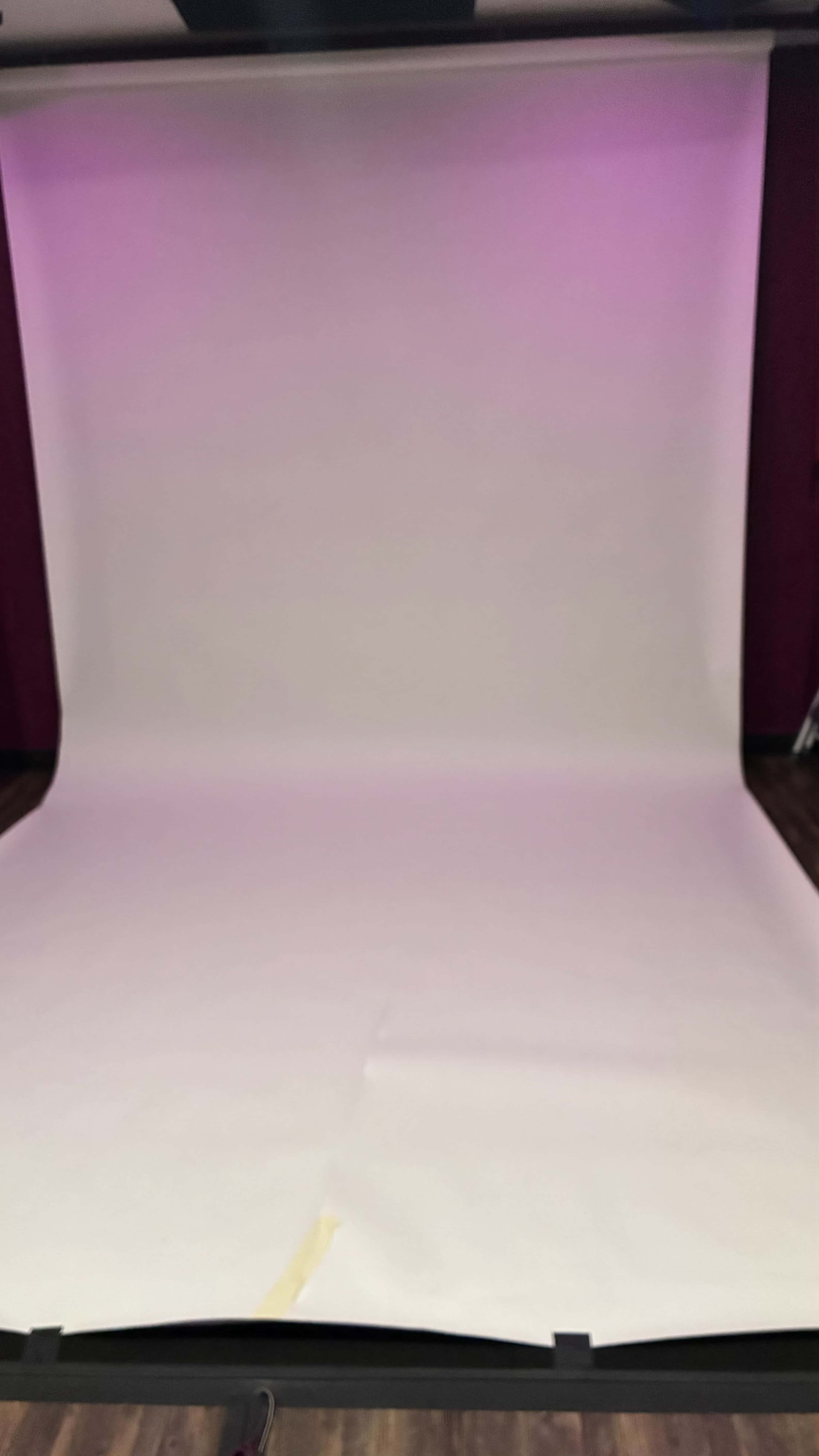 A smooth, light-colored backdrop is set up in a studio space with purple lighting.