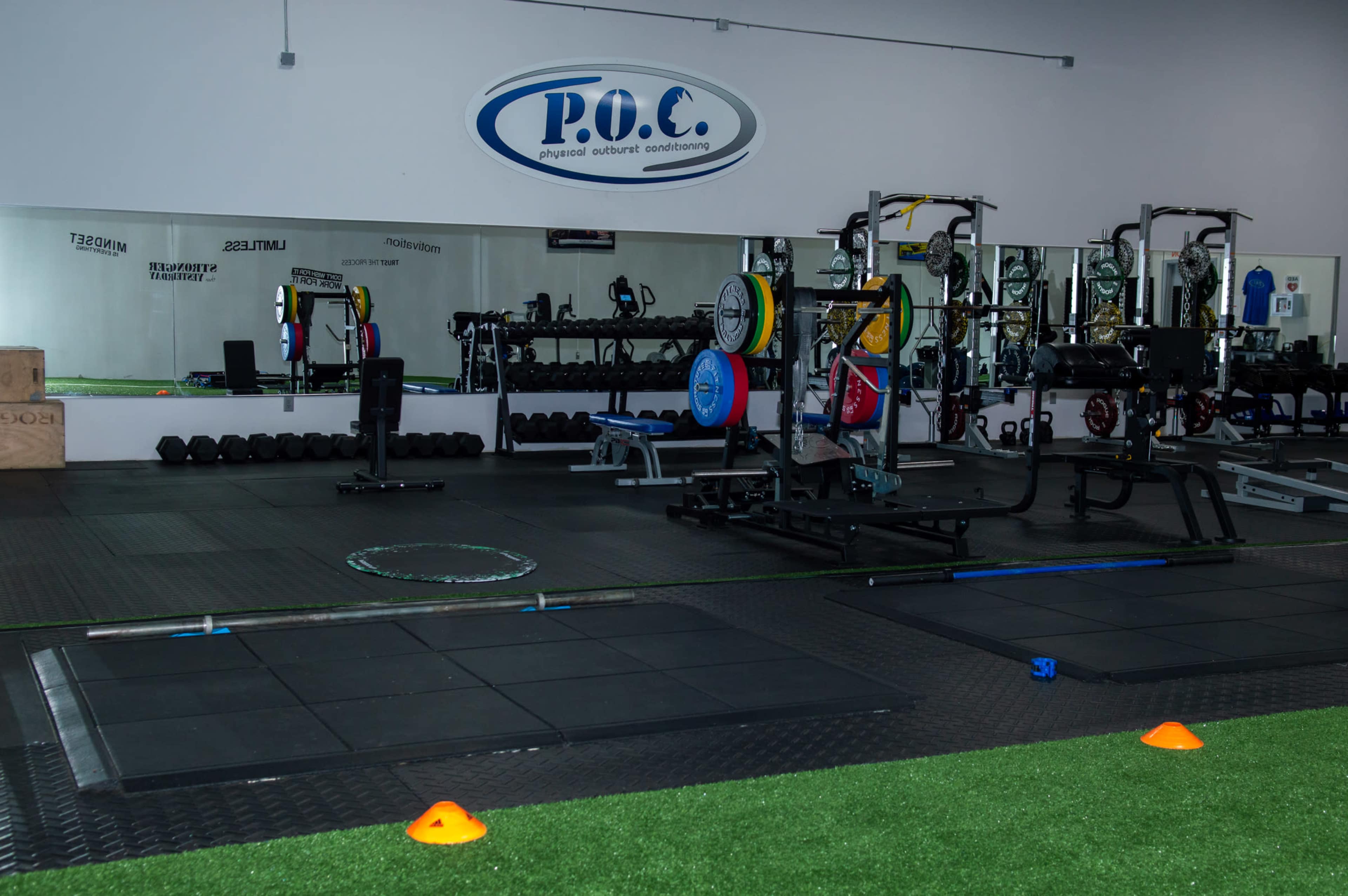 The image shows a gym interior equipped with weightlifting benches, barbells, and workout machinery, alongside mirrors and exercise mats.