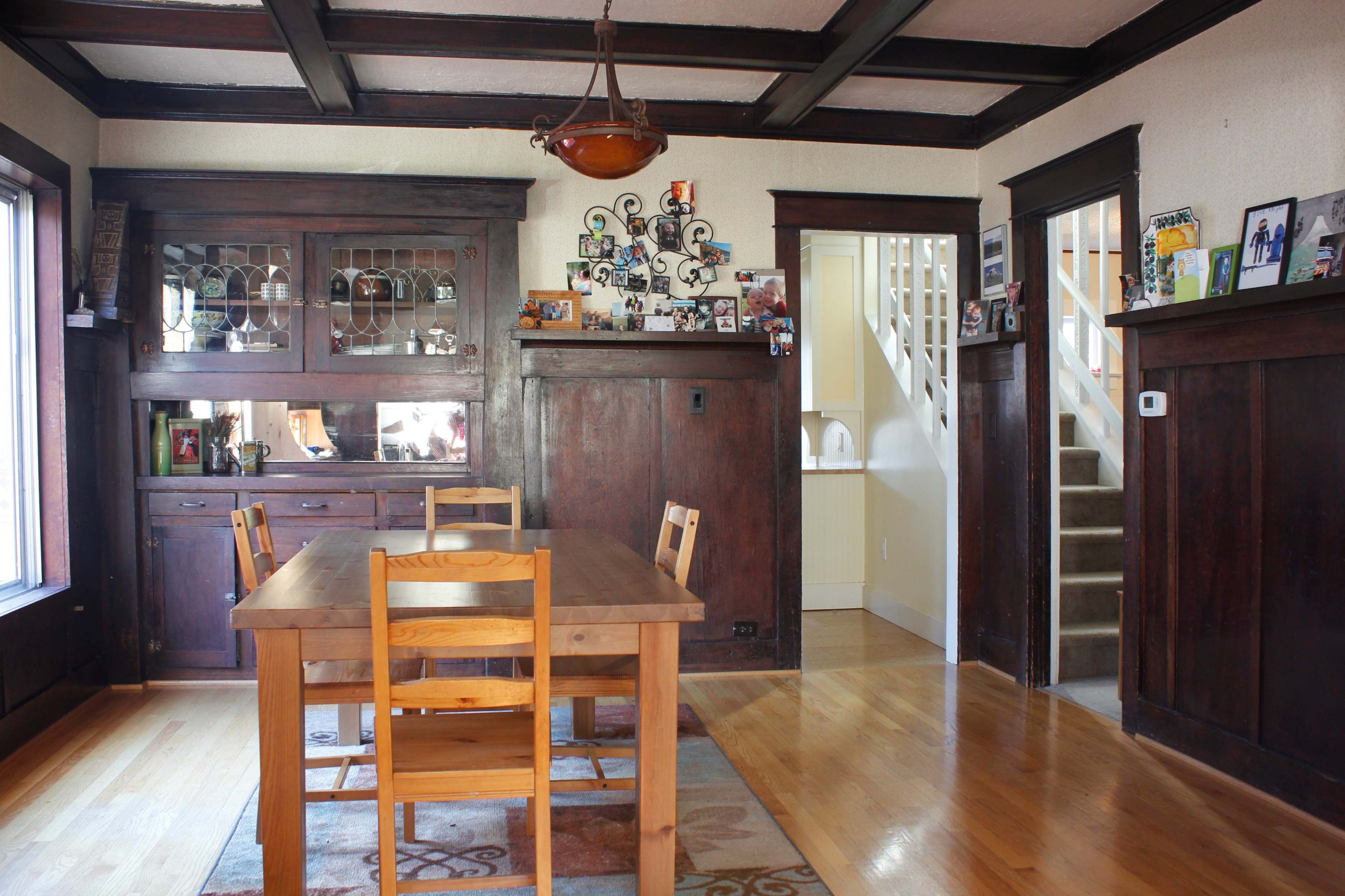 A dining area featuring a wooden table with four chairs, a sideboard against the wall, and a staircase leading to an upper level.