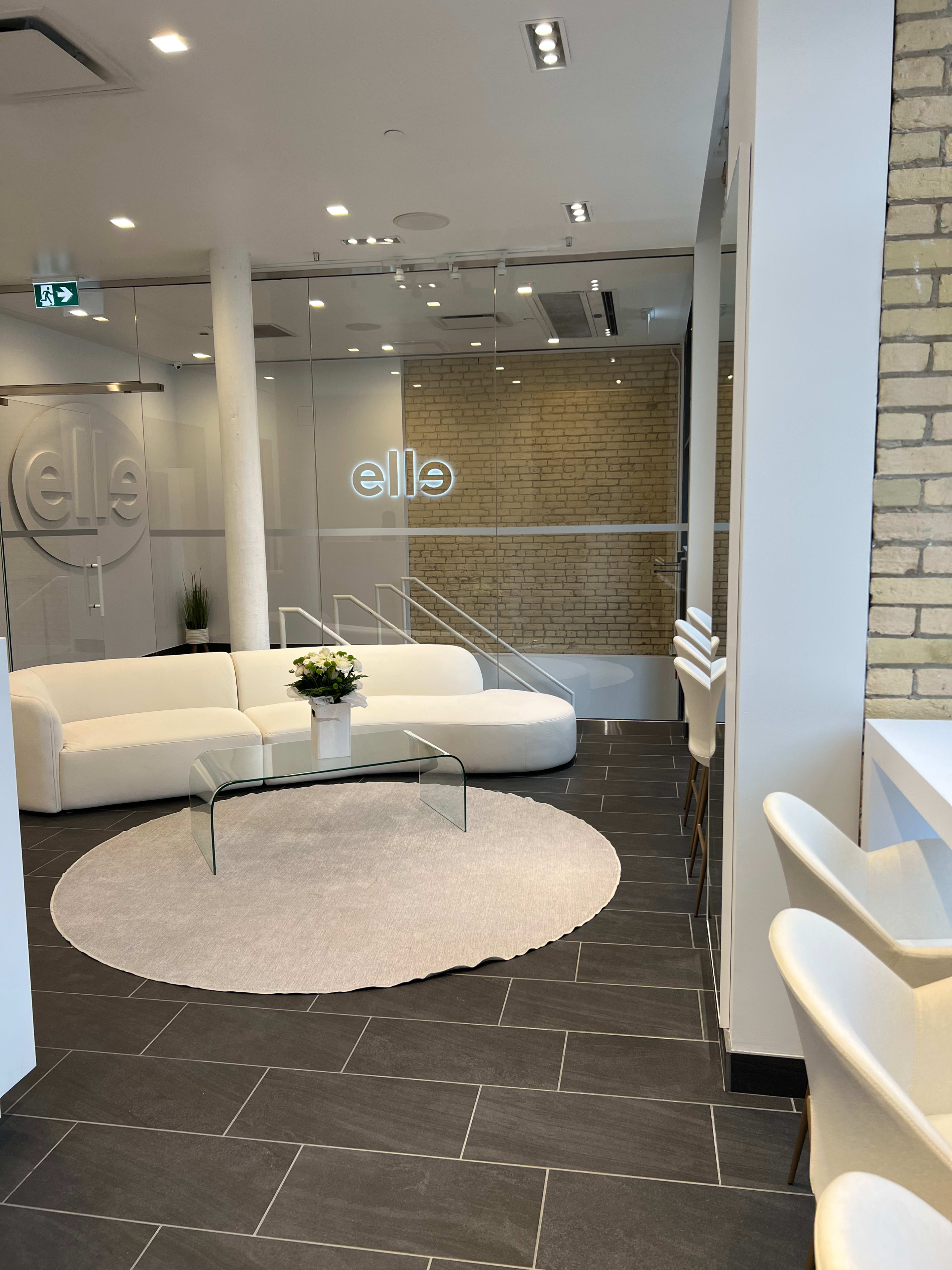 A modern interior of a reception area with a white sofa, a glass coffee table, and a circular rug on a dark tiled floor, featuring a brick wall and sleek decor.