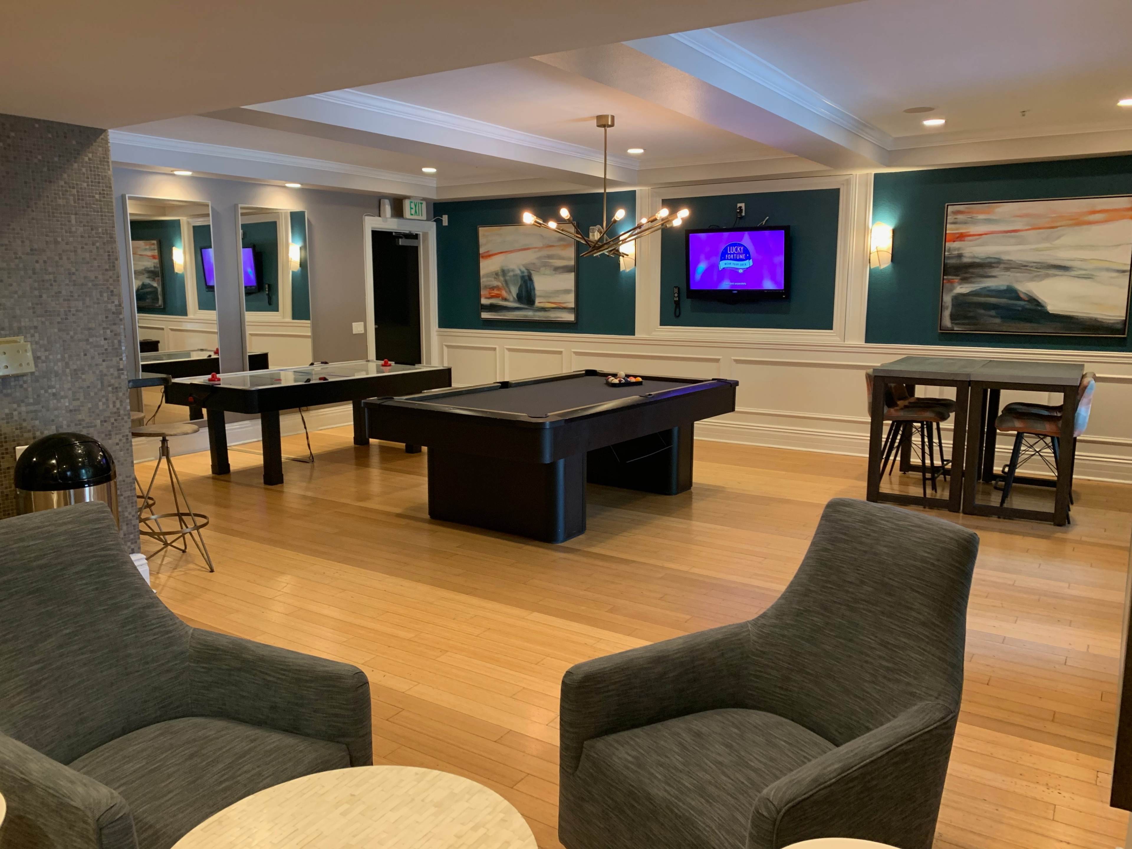 A recreational room featuring a pool table, a foosball table, two seating areas, and multiple wall-mounted televisions.