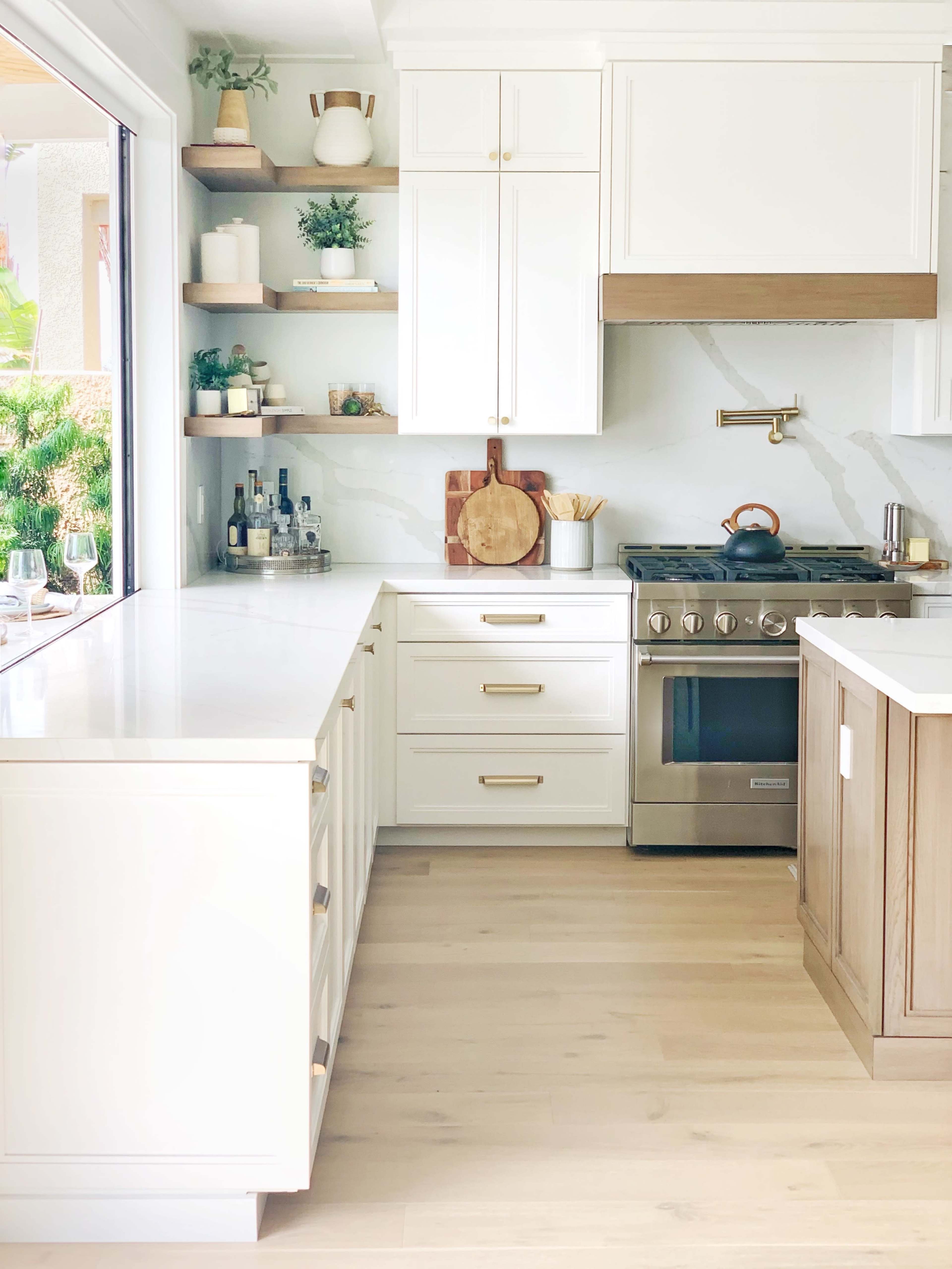 A modern kitchen featuring white cabinetry, a stainless steel oven, and wooden shelves filled with kitchen items.