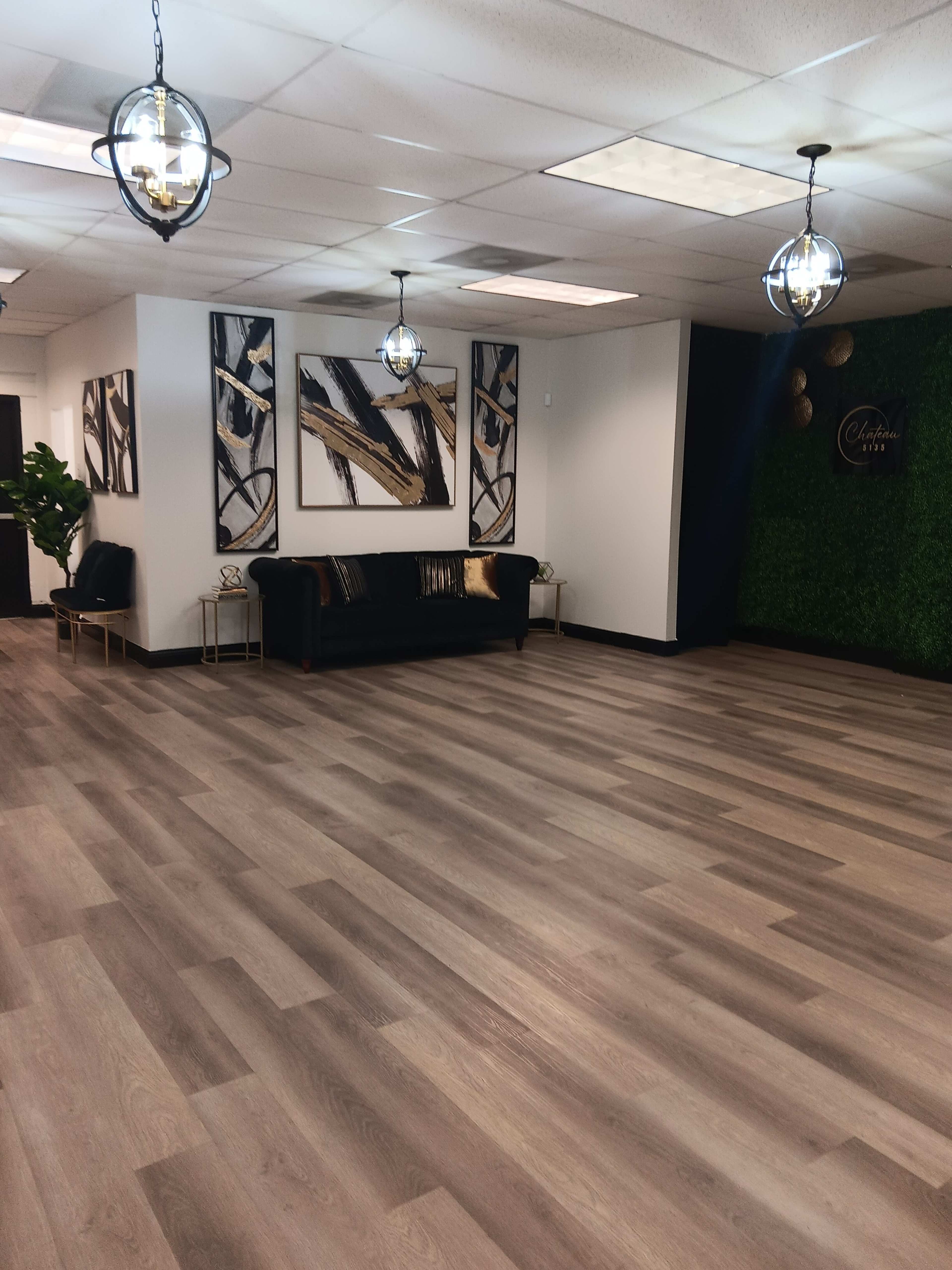 A modern indoor space with wooden flooring, a black couch, abstract wall art, and decorative hanging lights.