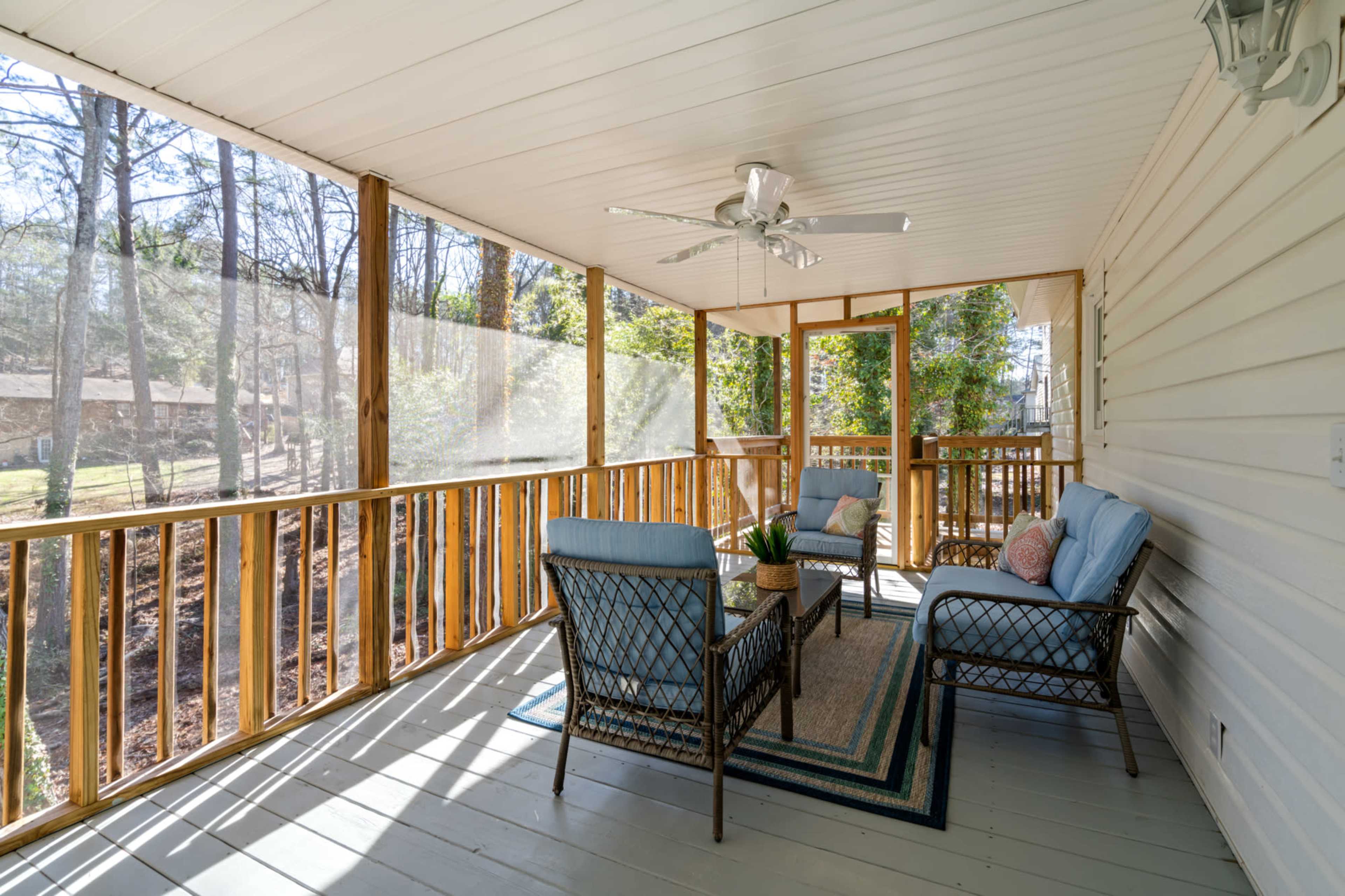 A screened-in porch featuring wicker furniture and a ceiling fan, surrounded by trees.