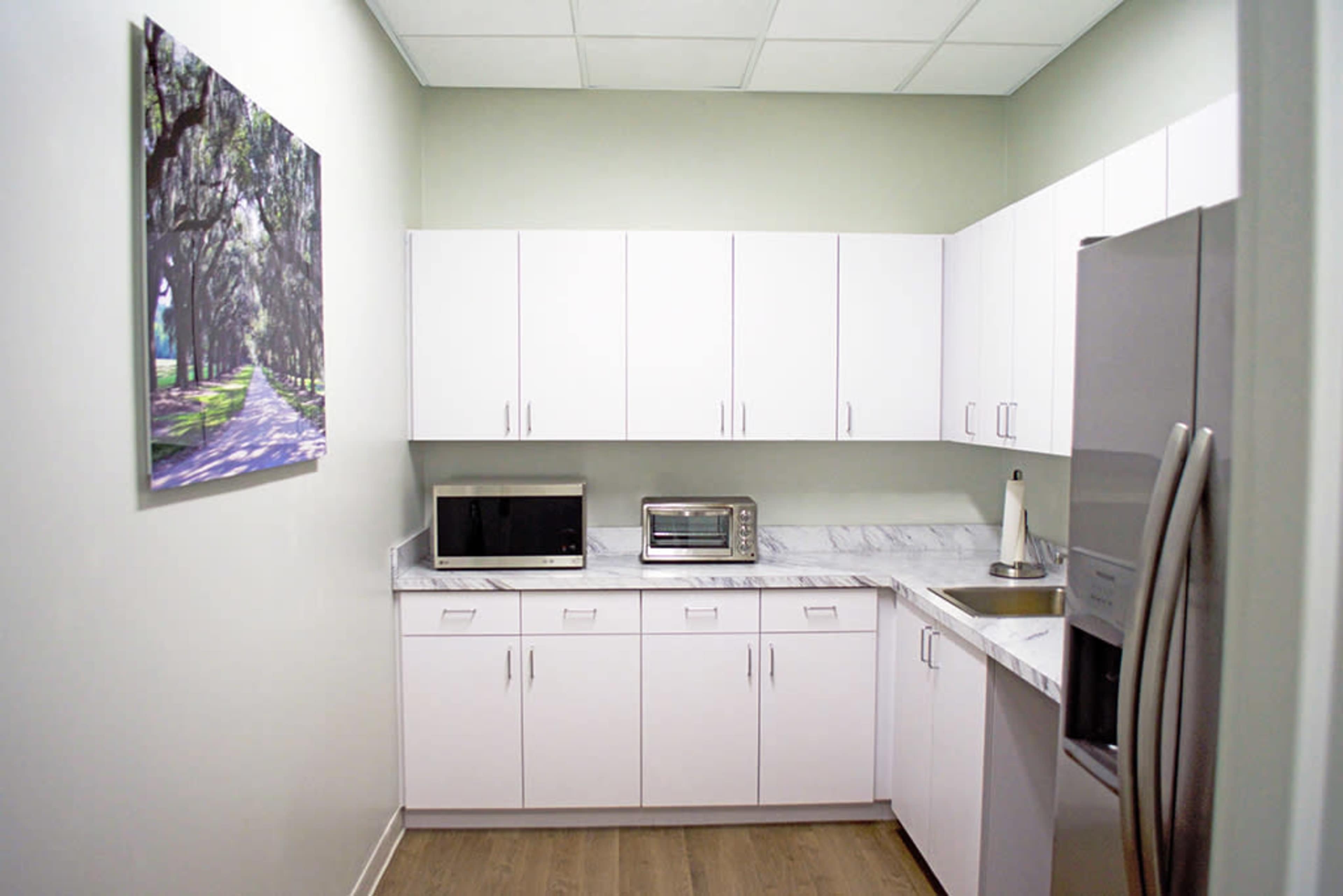 A modern kitchen with white cabinets, a microwave, a toaster oven, and a stainless steel refrigerator, set against a light green wall.