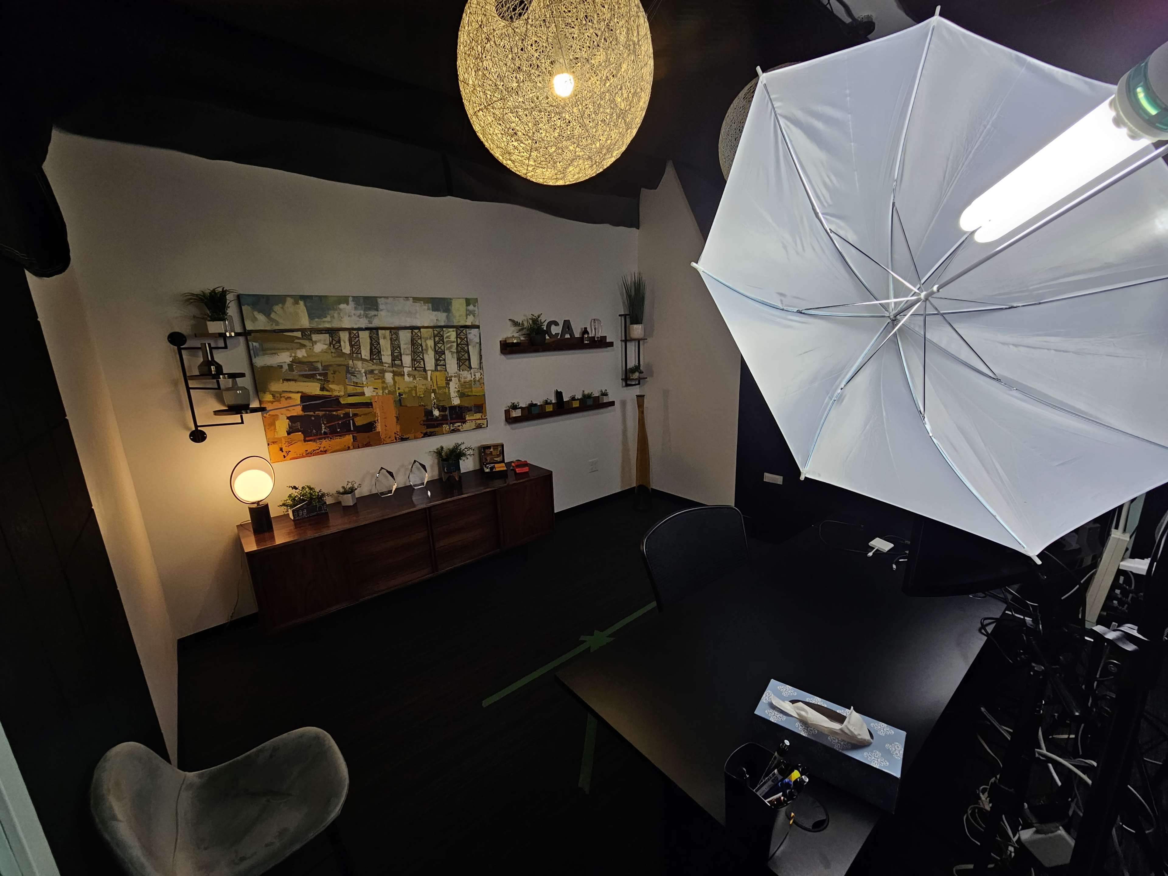 An office space with a dark wood desk, a chair, decorative shelves, and lighting fixtures, including an umbrella light setup.