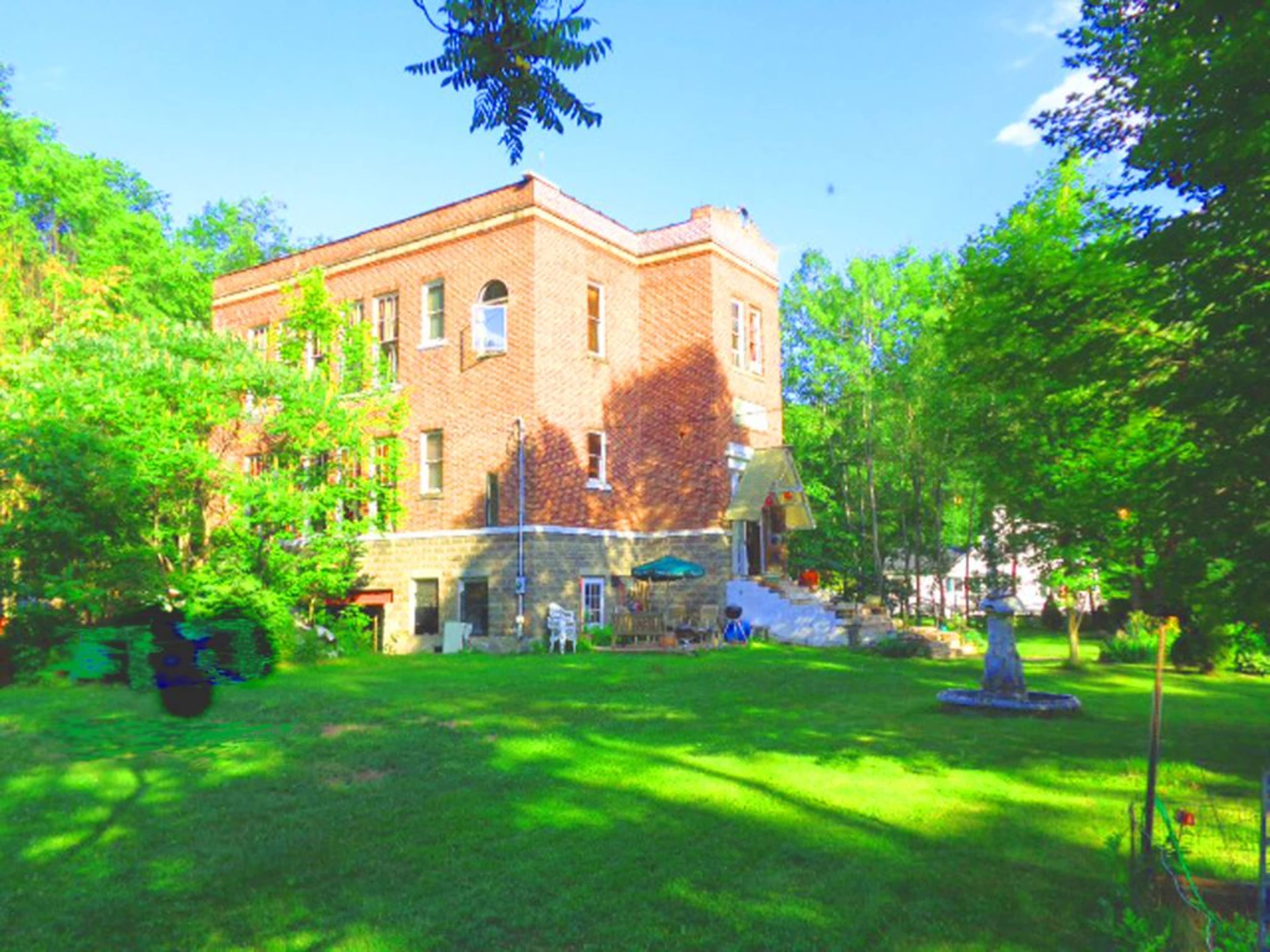 The image shows a large brick building surrounded by greenery and a well-maintained lawn.