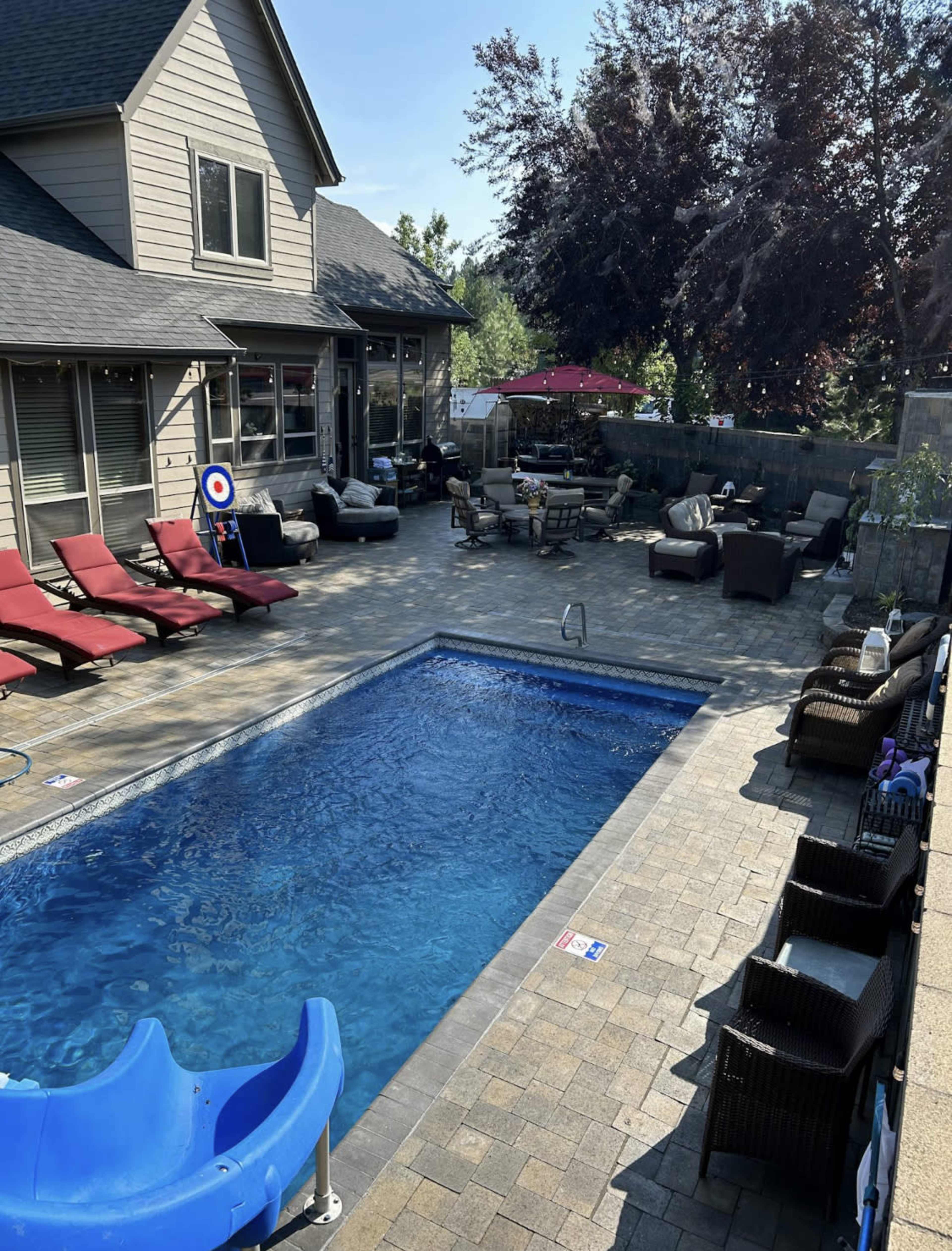 A backyard patio with a swimming pool, lounge chairs, and various seating areas surrounded by greenery.