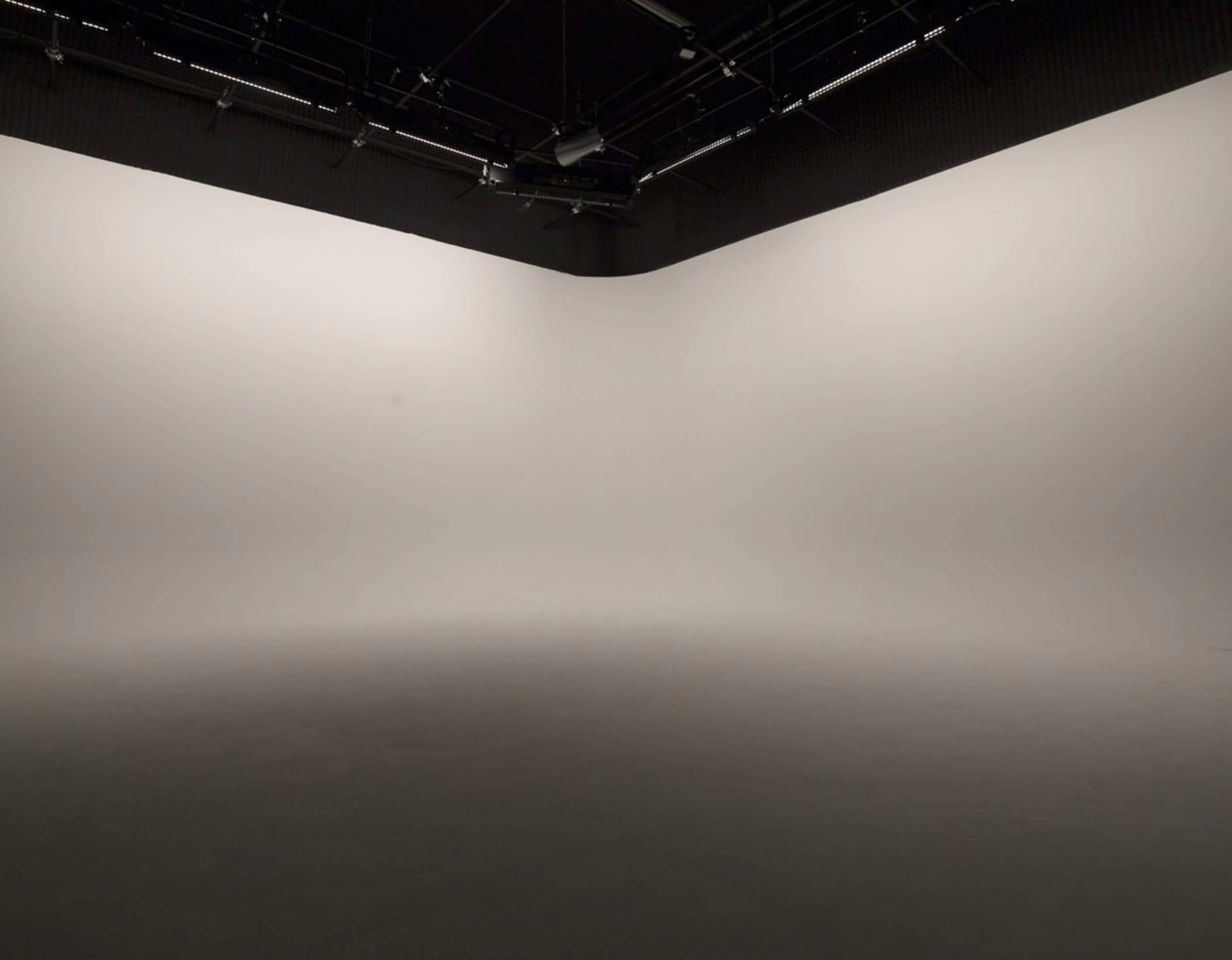 The image shows a large, empty studio space with plain, white walls and a dark floor.