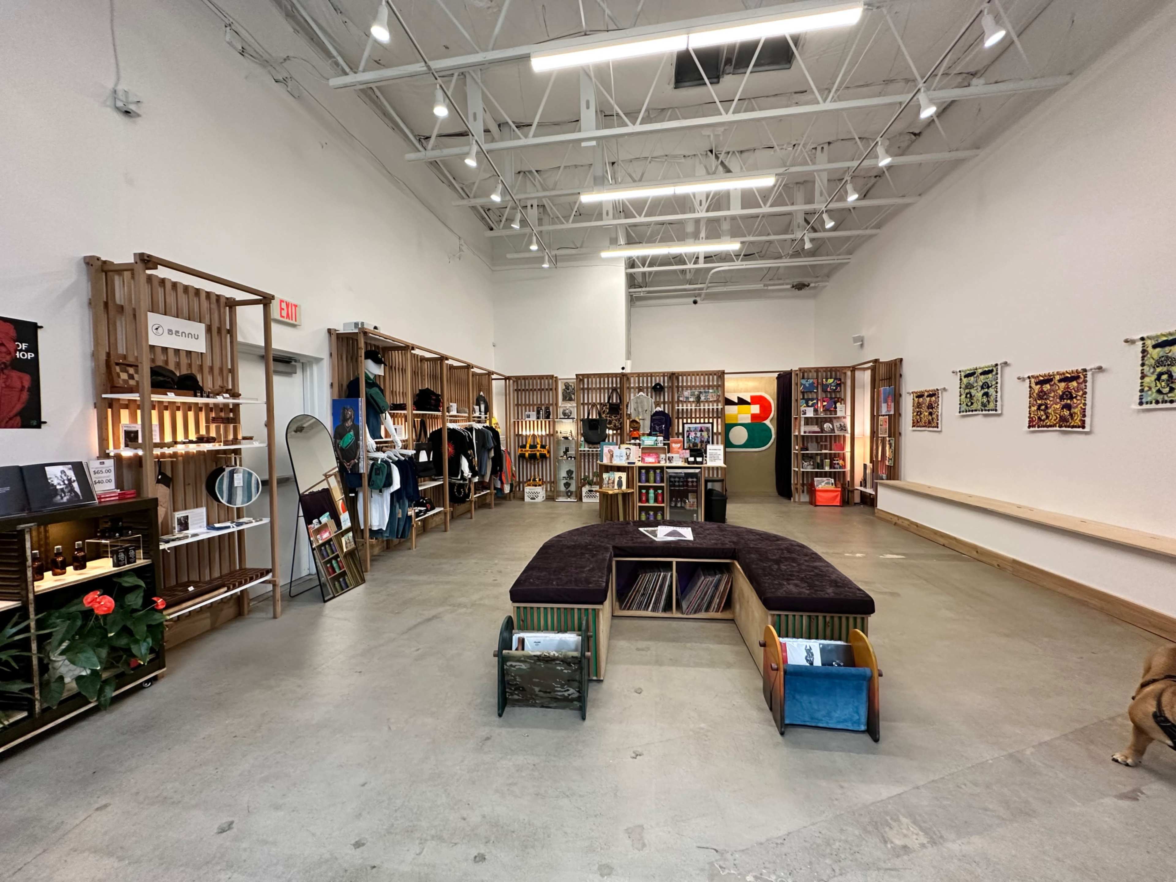 An interior of a retail space featuring wooden display shelves filled with various products, a central seating area, and clothing racks along the walls.