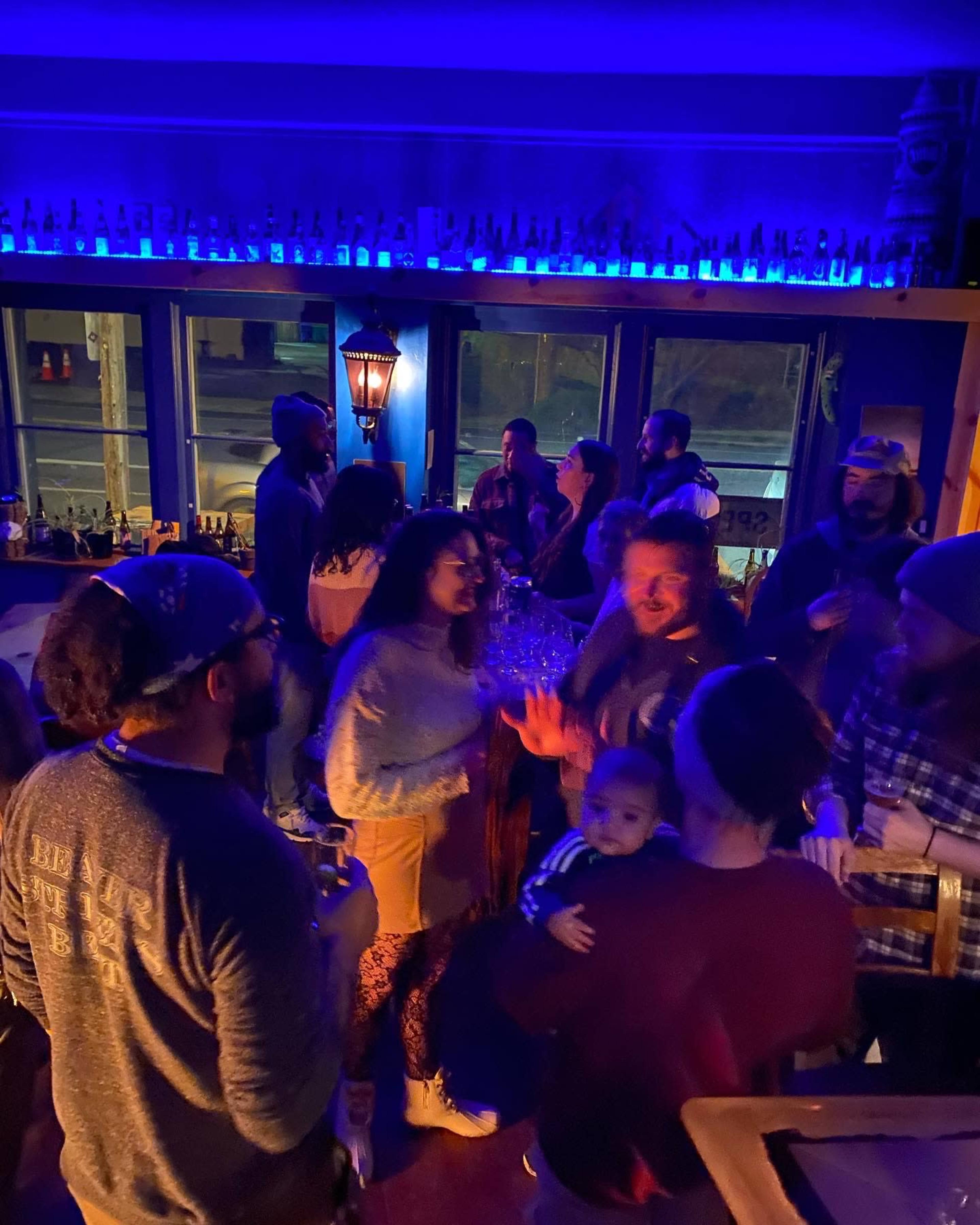 A group of people socializes and drinks in a dimly lit bar with blue lighting.