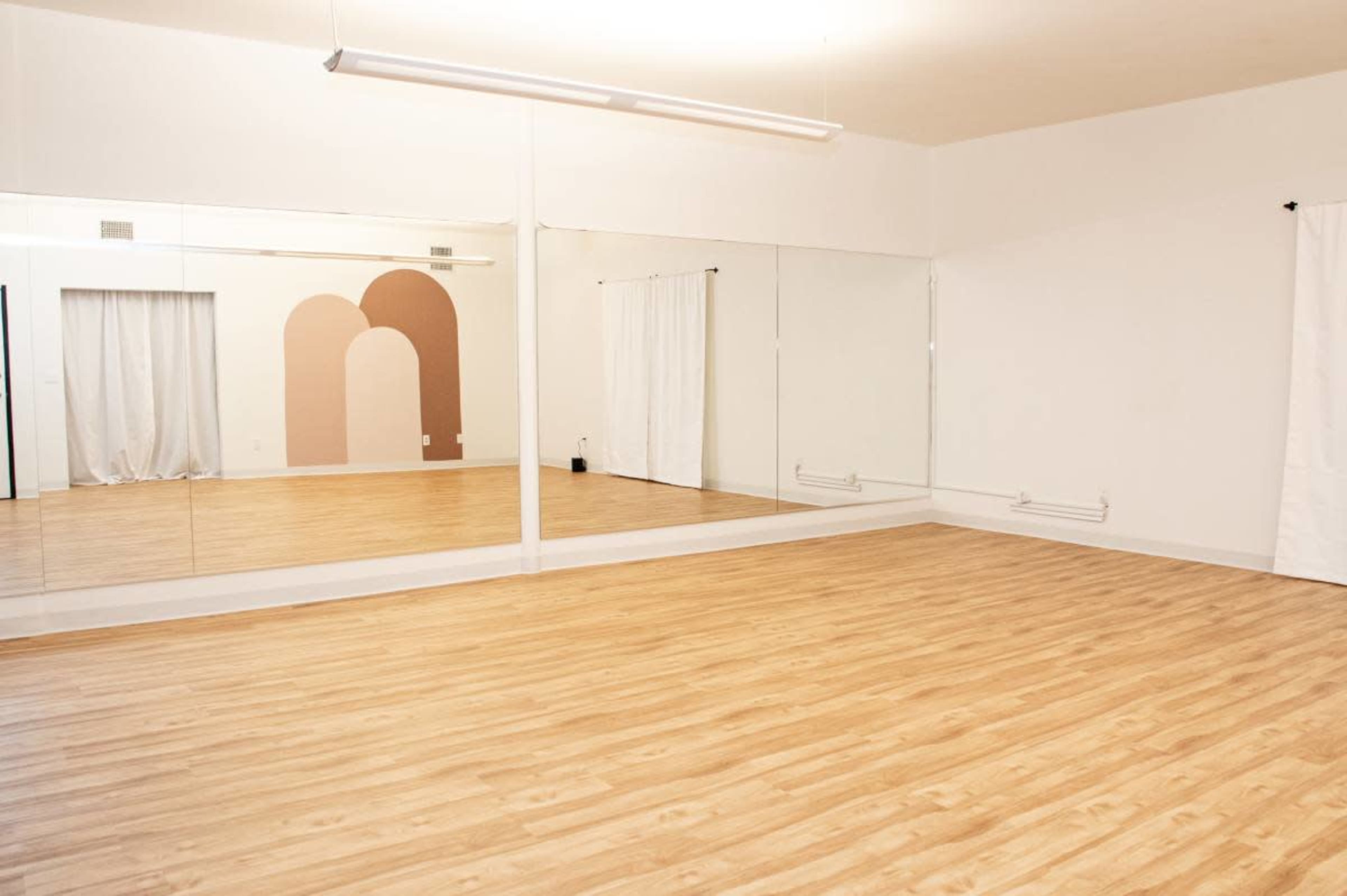 The image shows a spacious, empty room with wooden flooring and large mirrors on one wall.