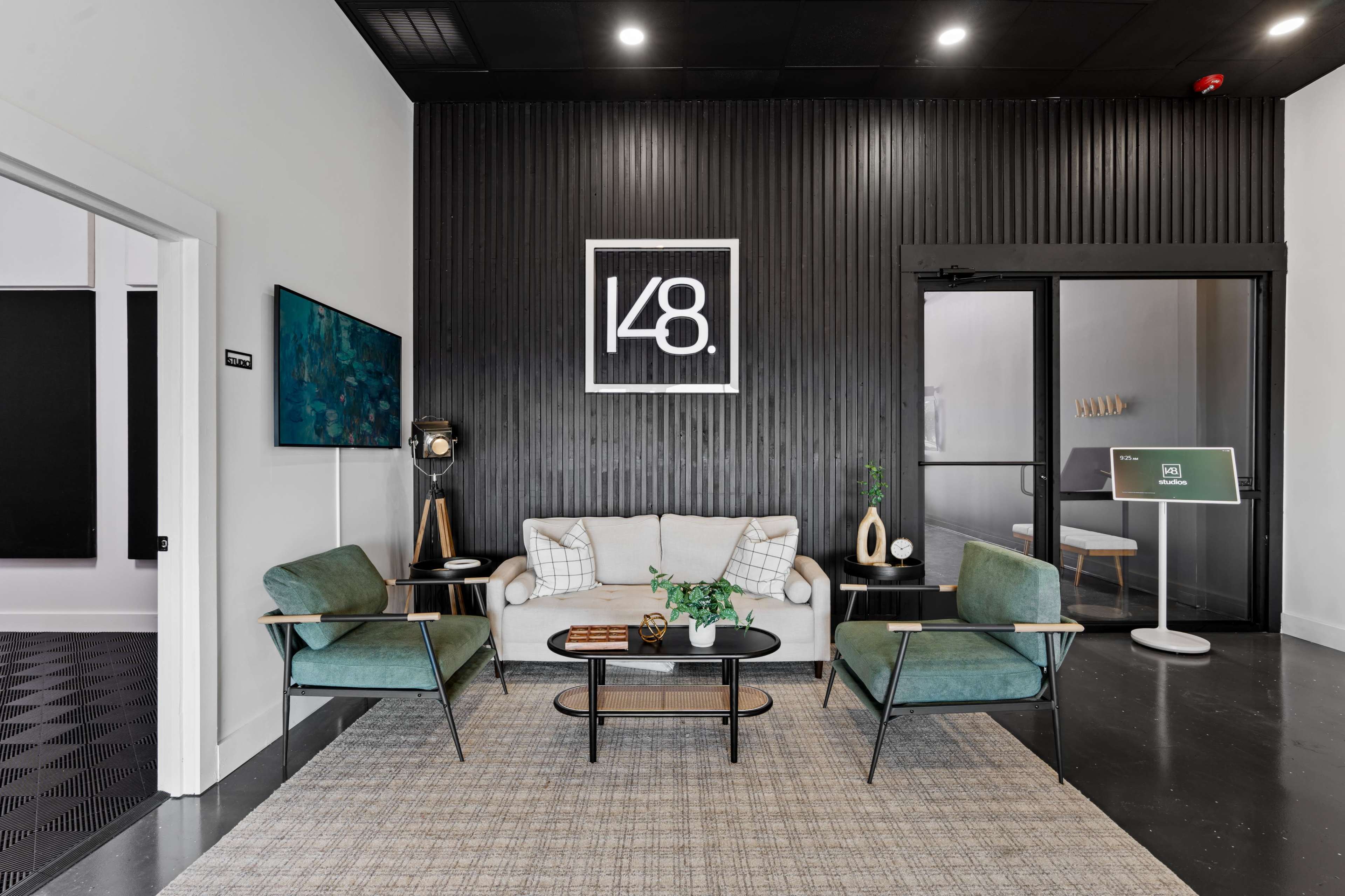 The image shows a modern reception area with a sofa, two chairs, a coffee table, and a large wall-mounted logo in a minimalist design.