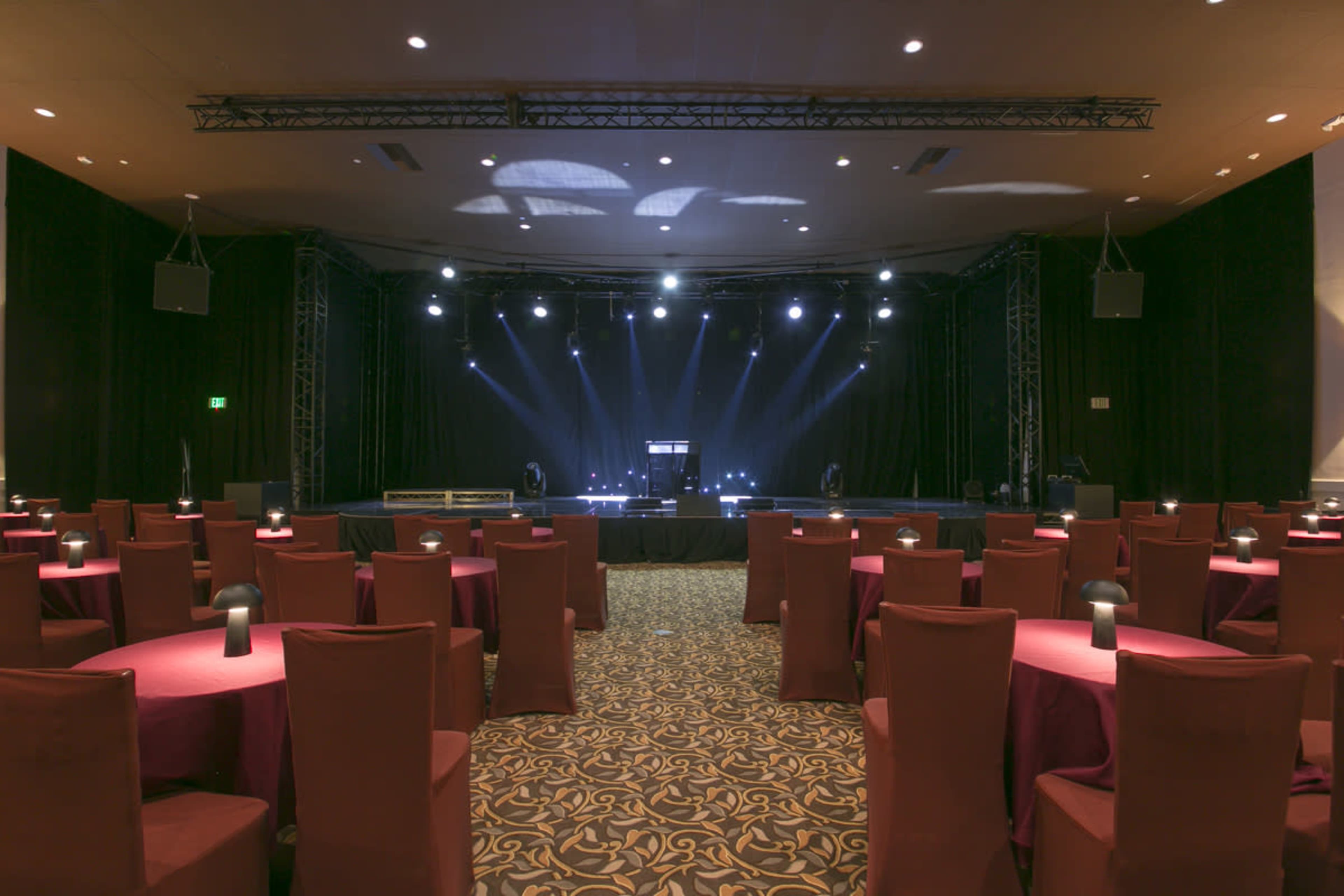 A performance stage with lighting set up in a room filled with round tables and chairs.