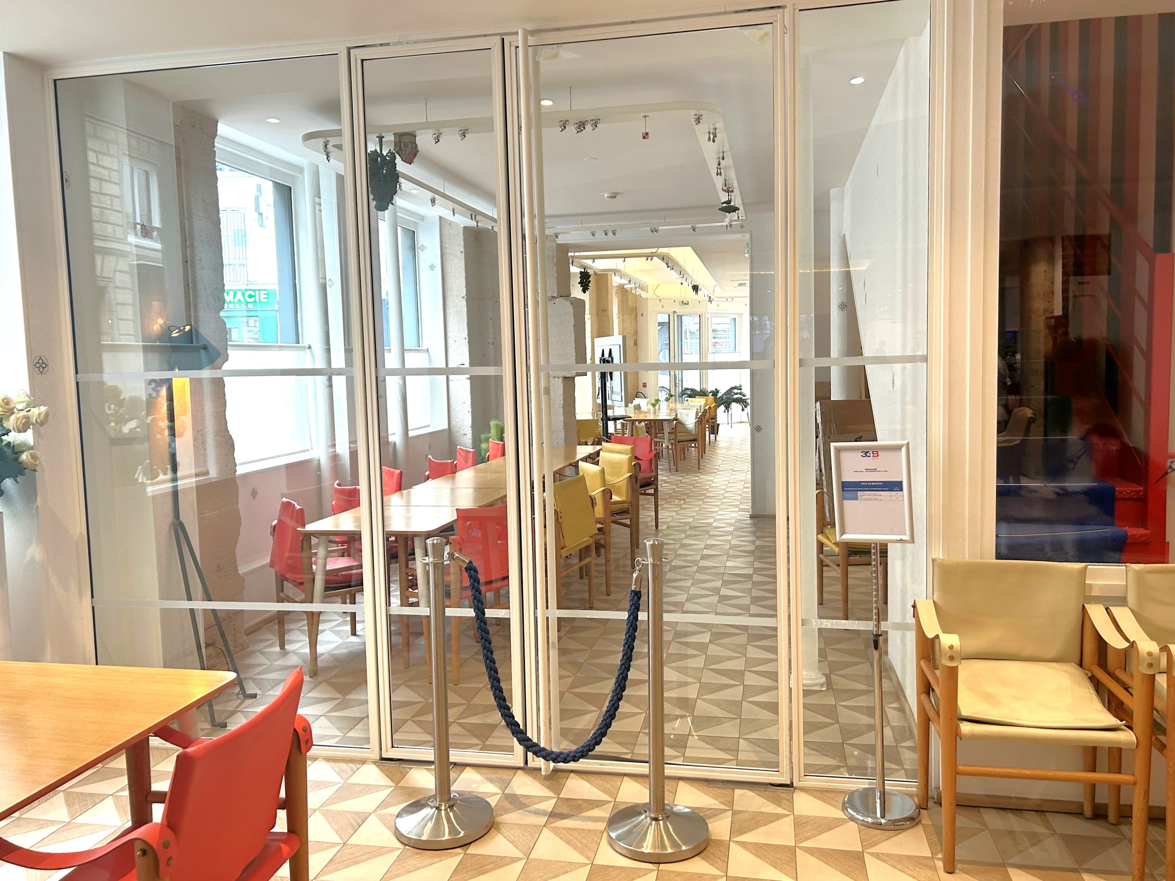 A glass entrance to a modern dining area with wooden tables and red chairs.