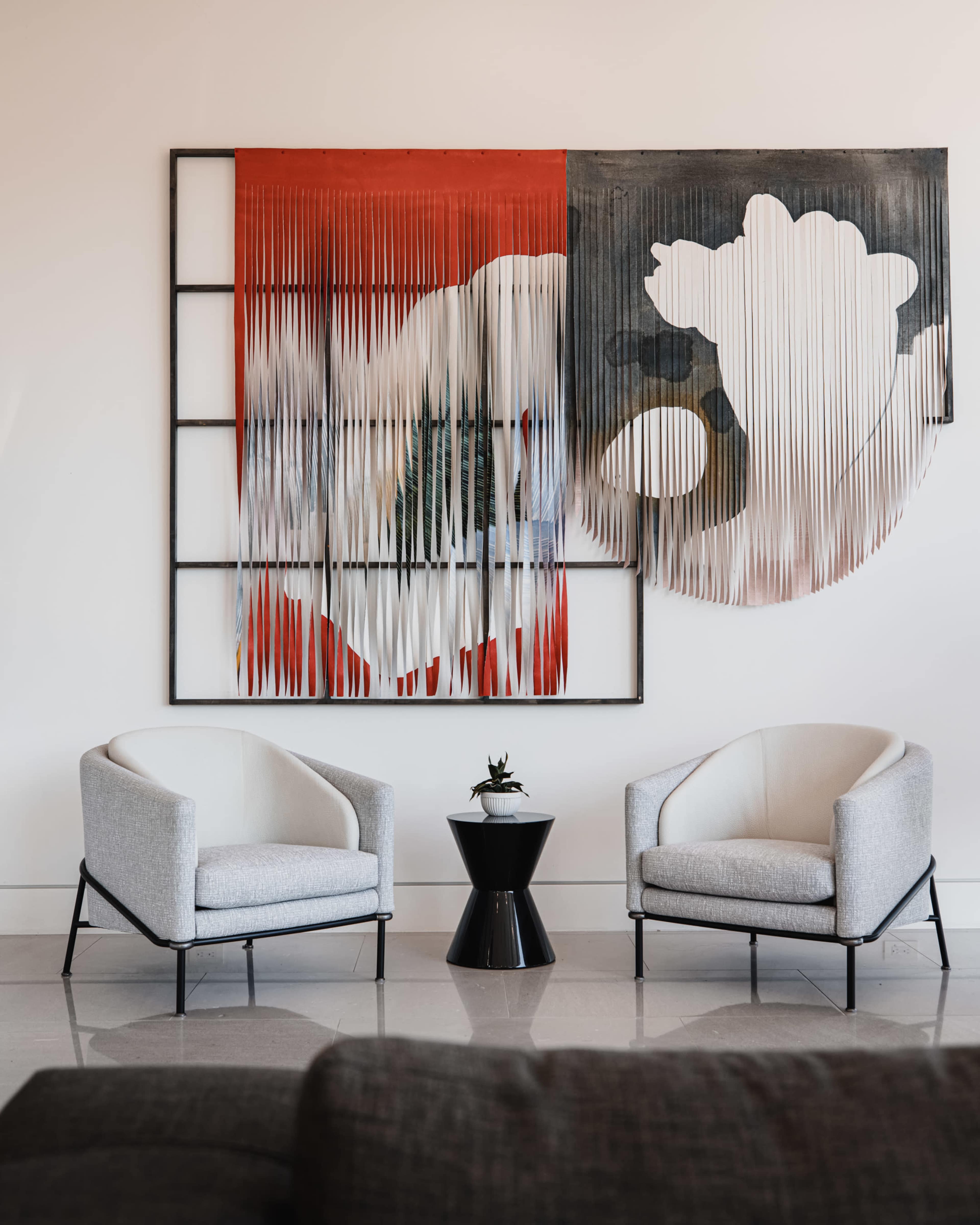 A modern seating area features two gray upholstered chairs beside a black side table, with an abstract artwork on the wall above.