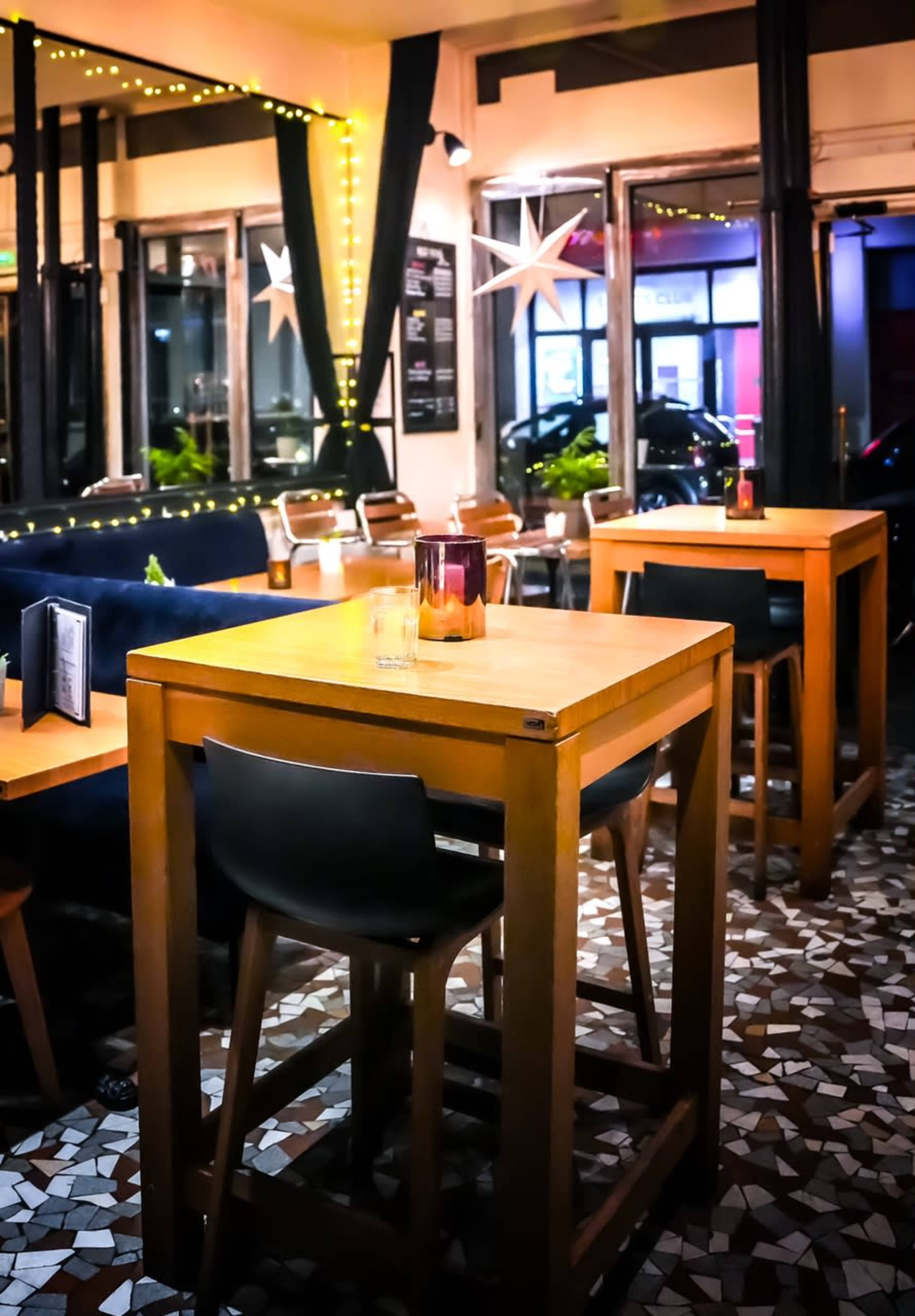 A restaurant interior with wooden tall tables and chairs, ambient lighting, and a tiled floor.