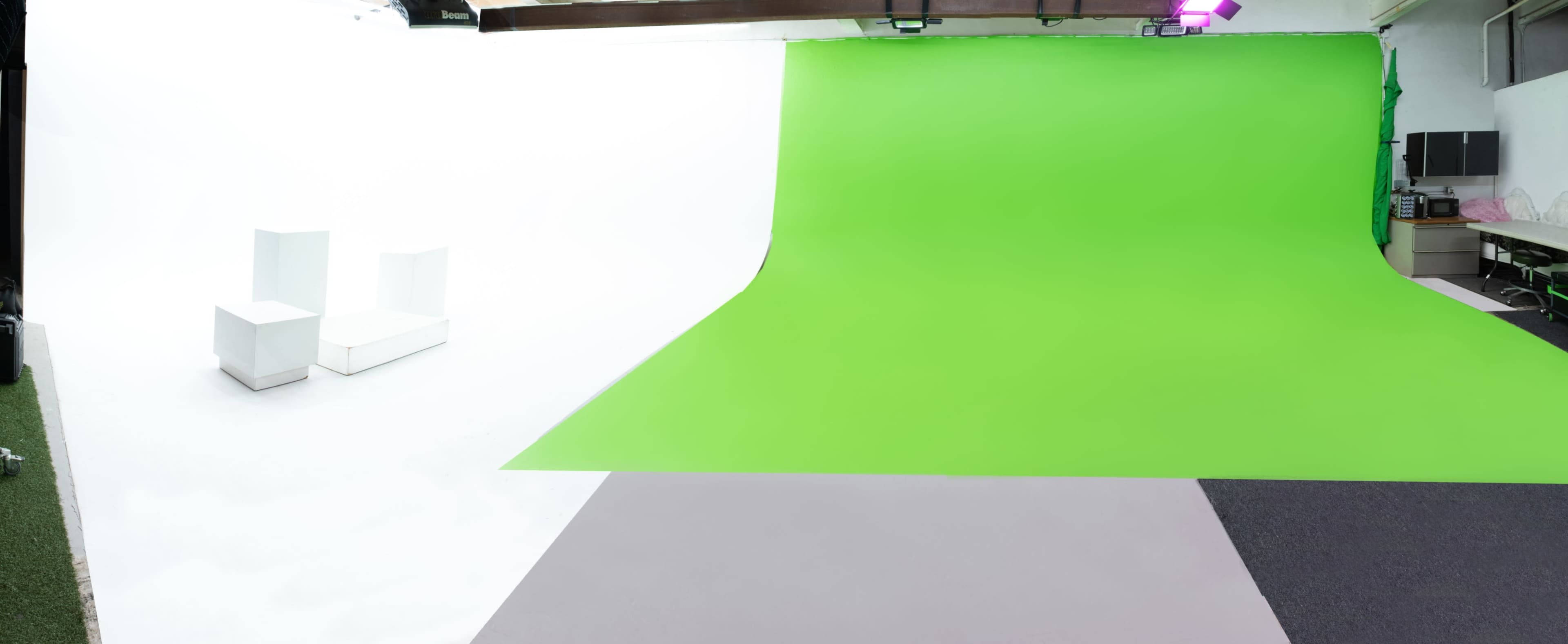 A photography studio featuring a green backdrop, white walls, and a light gray floor, with two white chairs positioned on one side.