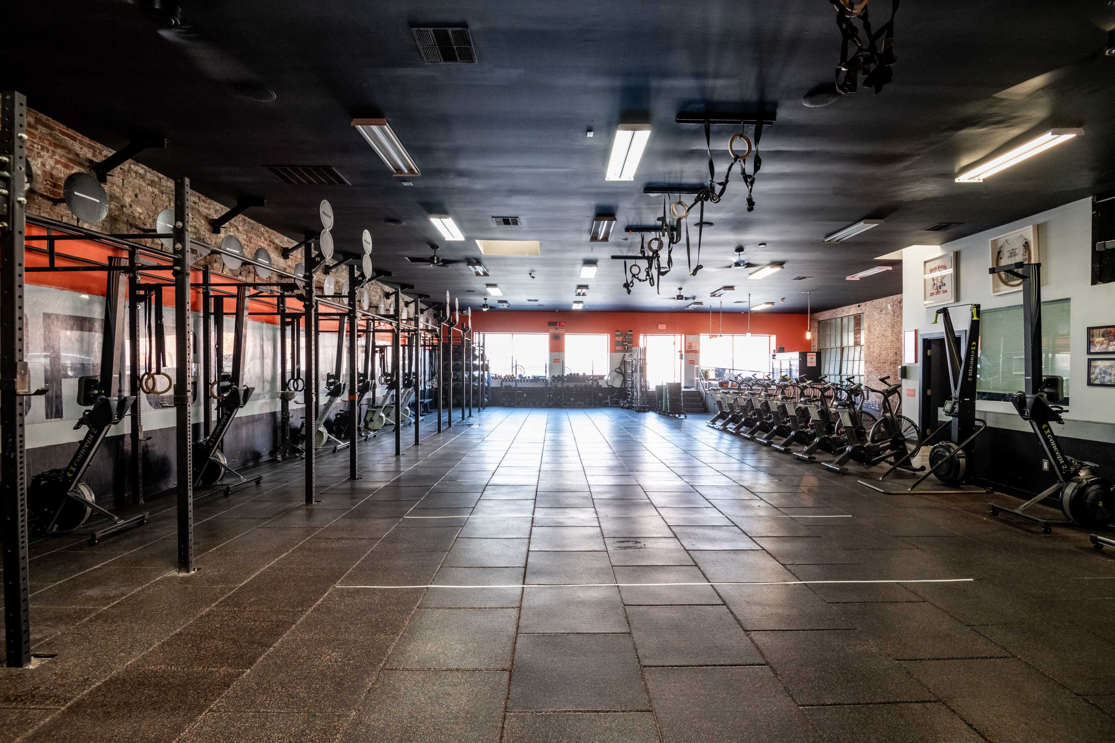 The image shows a spacious gym interior with exercise equipment arranged along the walls, including rowing machines and pull-up bars.
