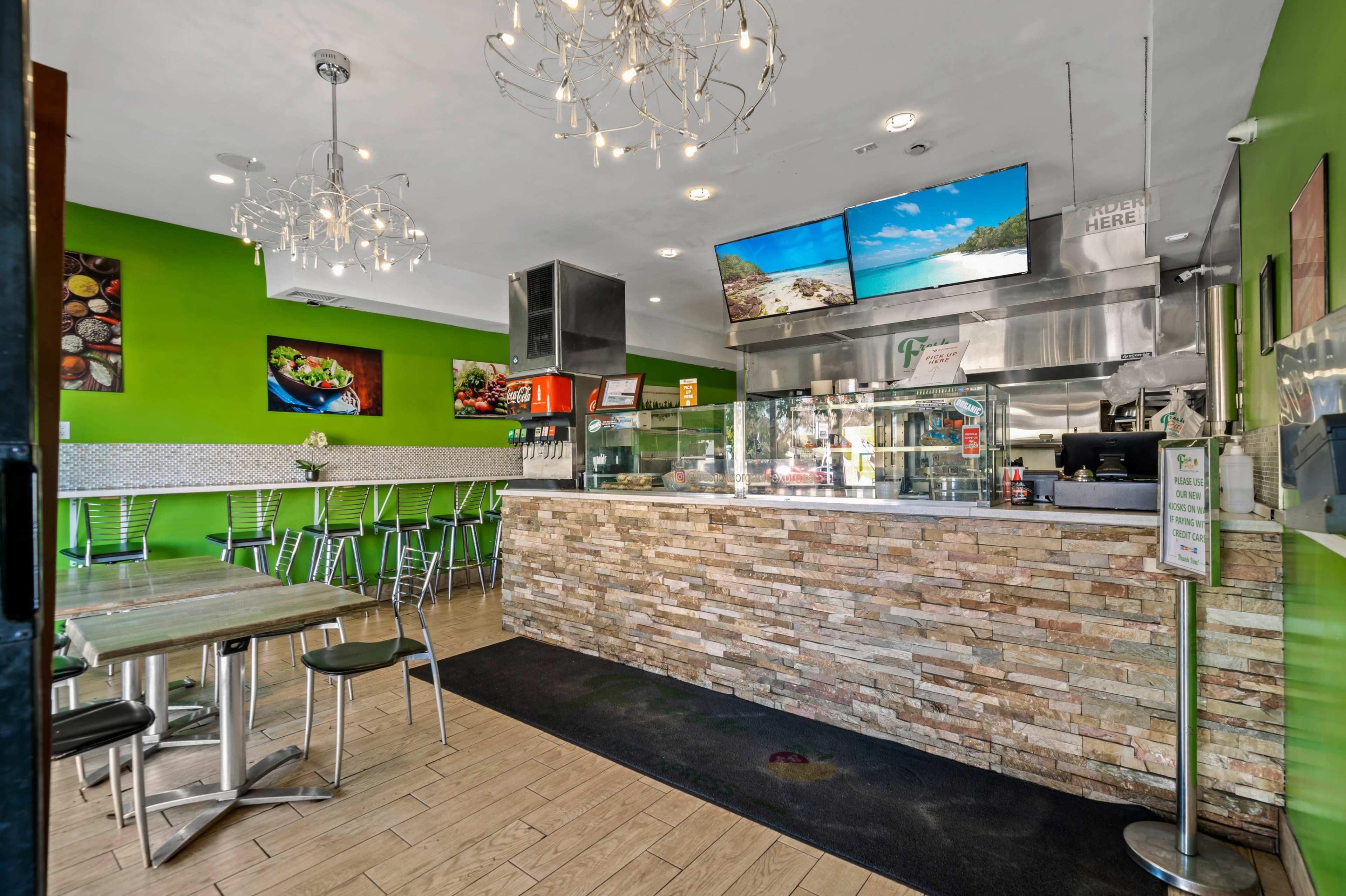 The interior of a brightly colored restaurant features modern decor, a stone counter, and multiple screens displaying images.