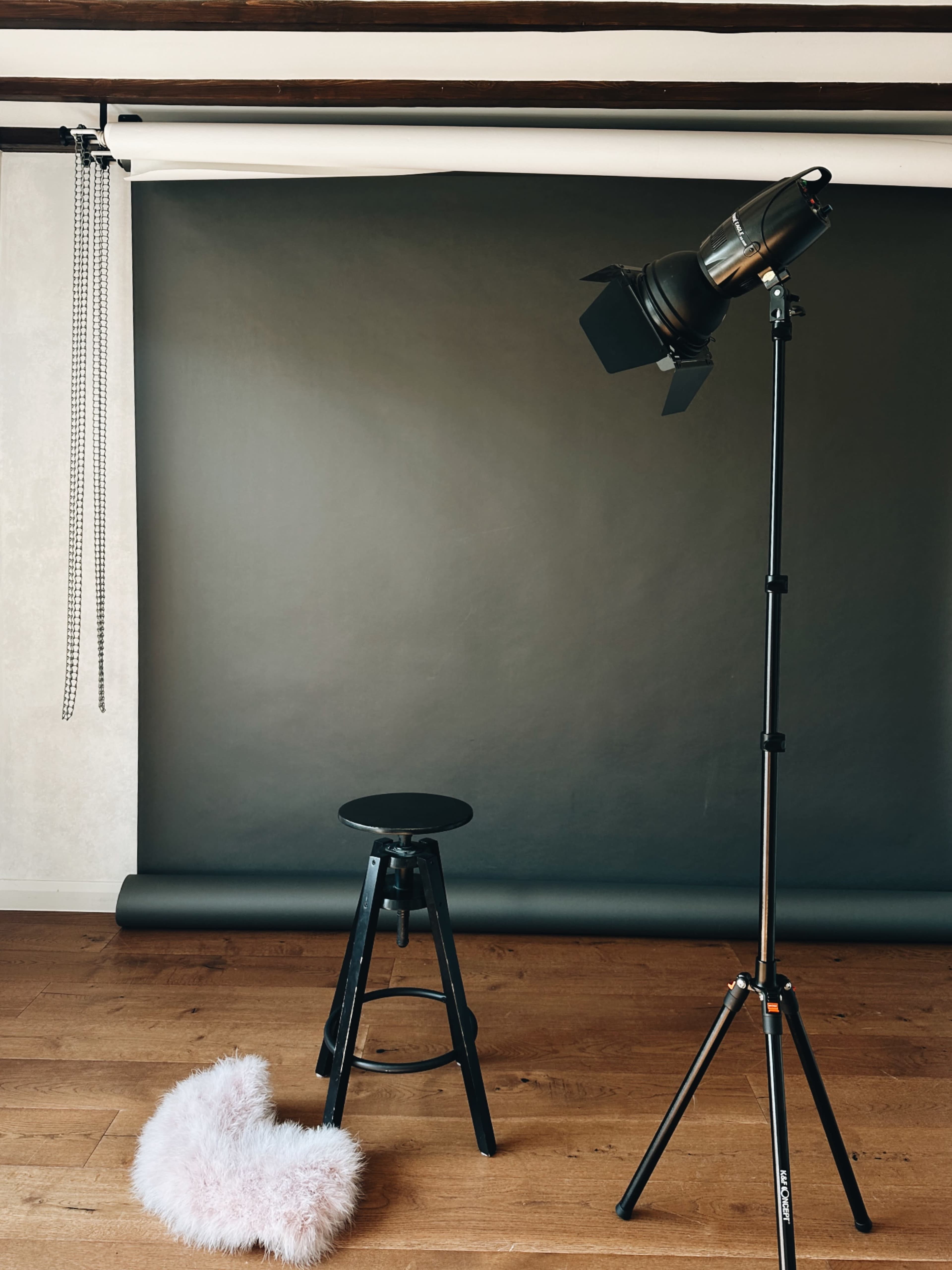 A black stool and a fluffy heart-shaped prop positioned in front of a dark backdrop with a studio light on a stand.