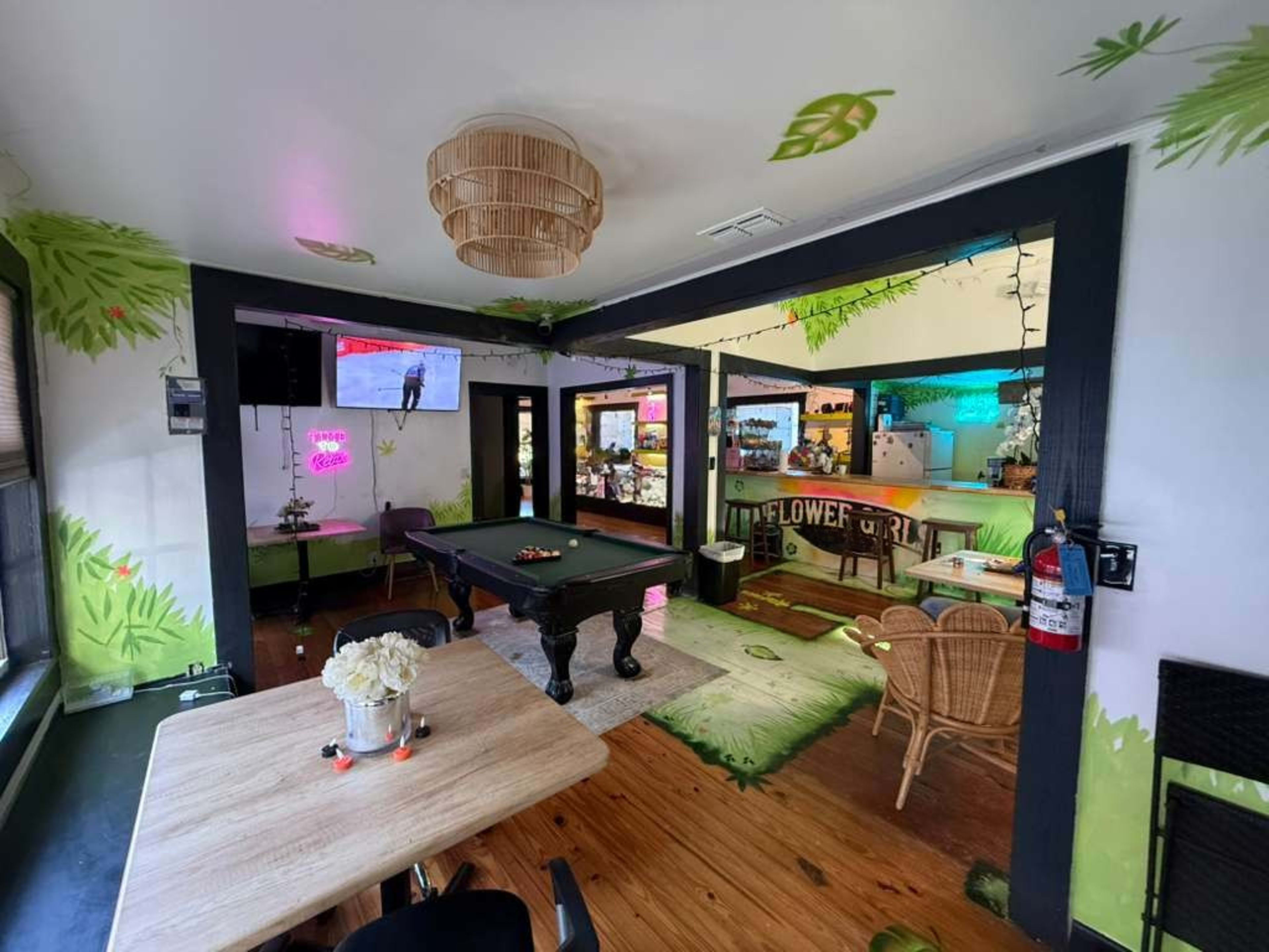 The image shows a cozy recreational room with a pool table, surrounded by vibrant green wall decorations and a well-lit bar area in the background.