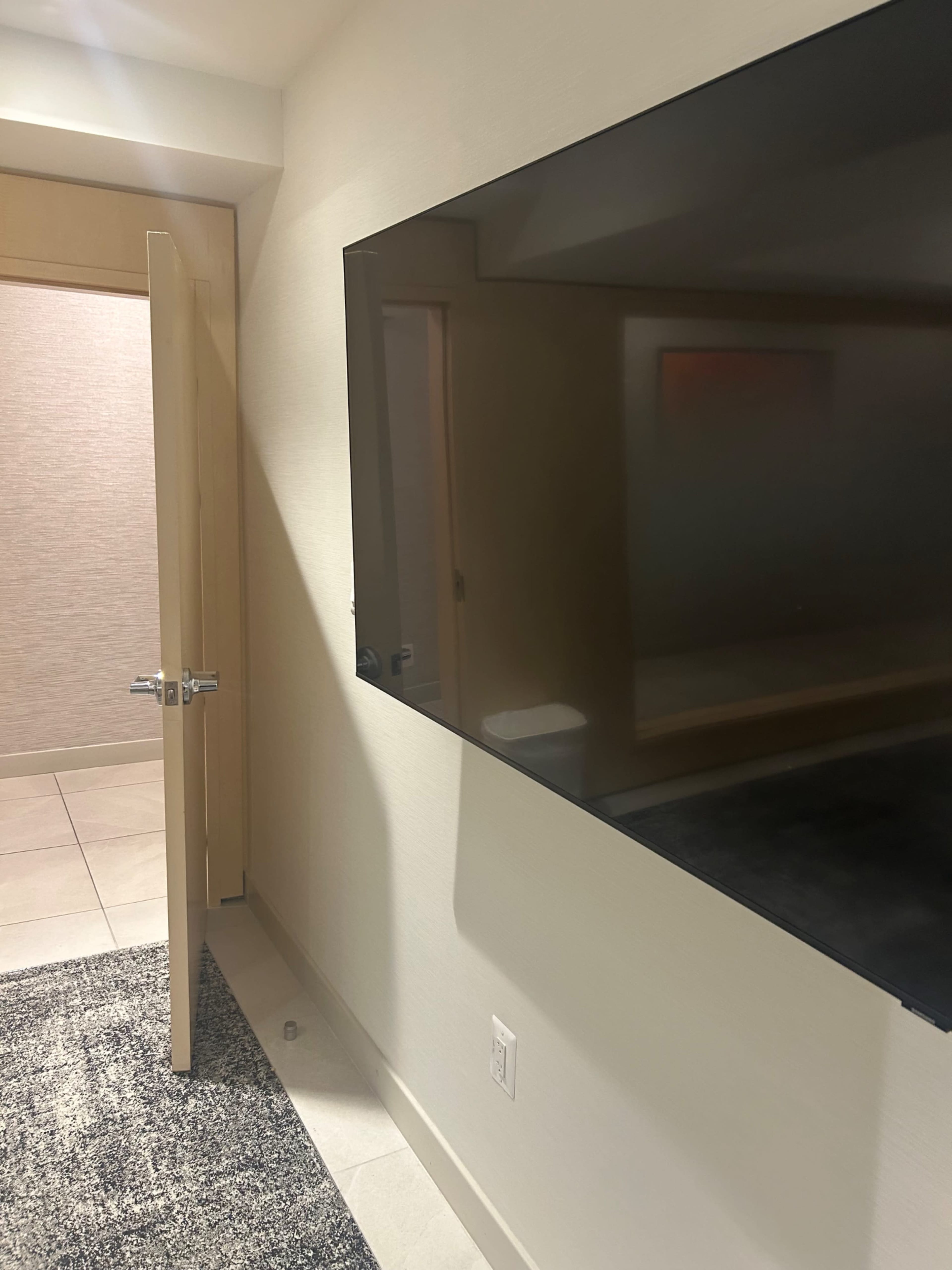 The image shows a modern room with a large flat-screen TV mounted on the wall beside a partially open door.