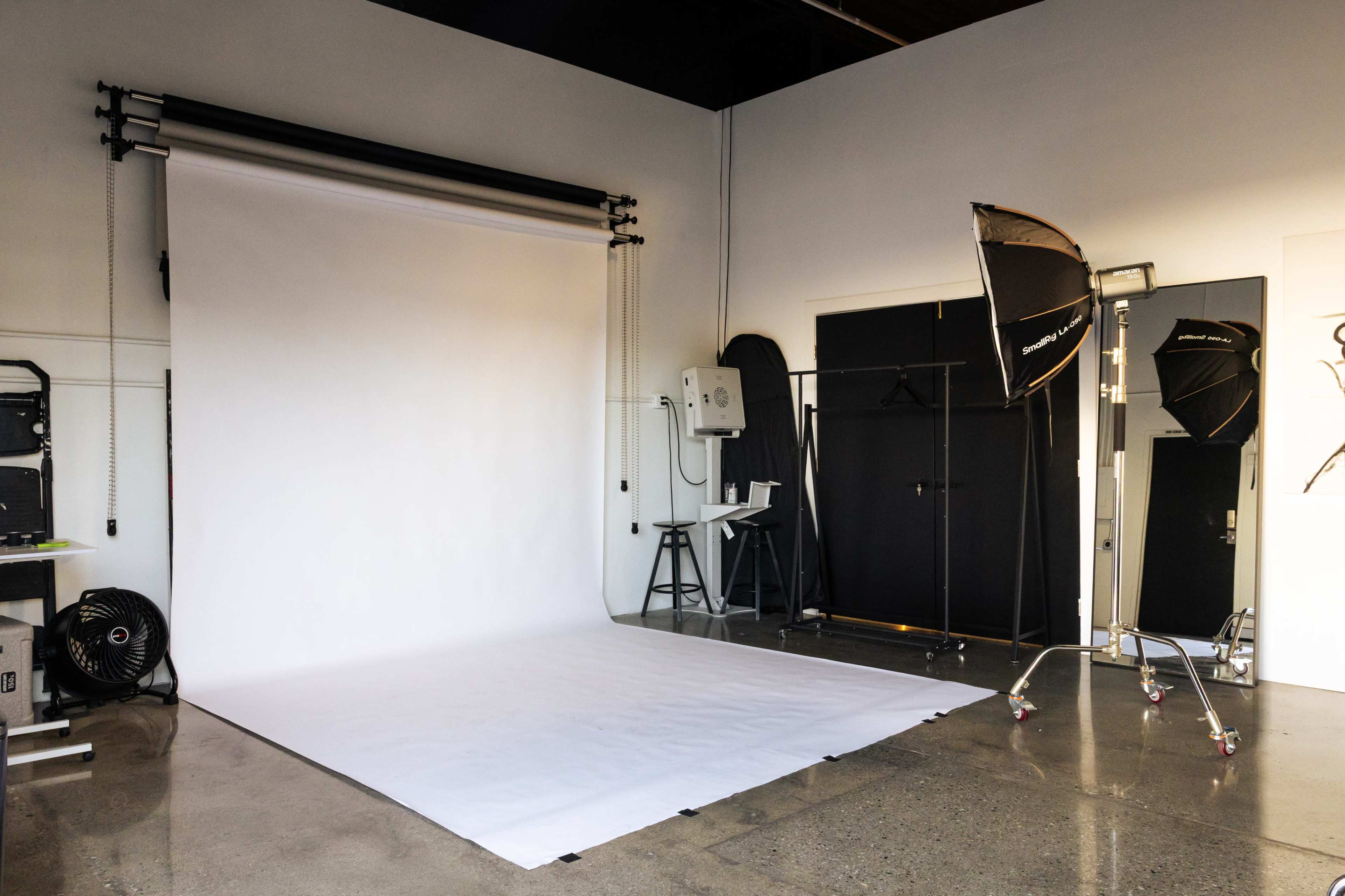 A photography studio features a white backdrop, studio lighting equipment, and a chair in a spacious, well-lit environment.