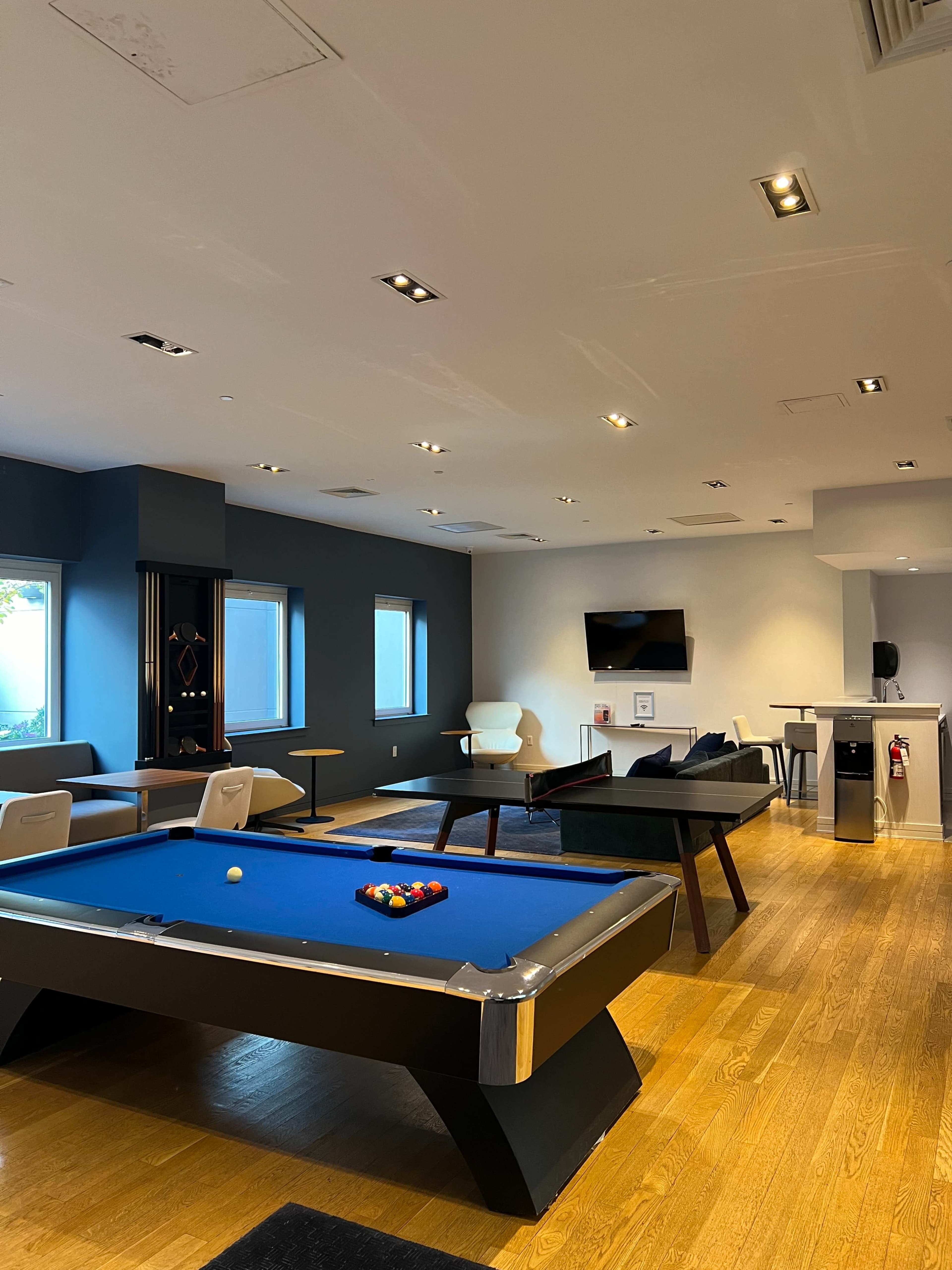 A modern game room featuring a blue pool table, a seating area, and a television on the wall.