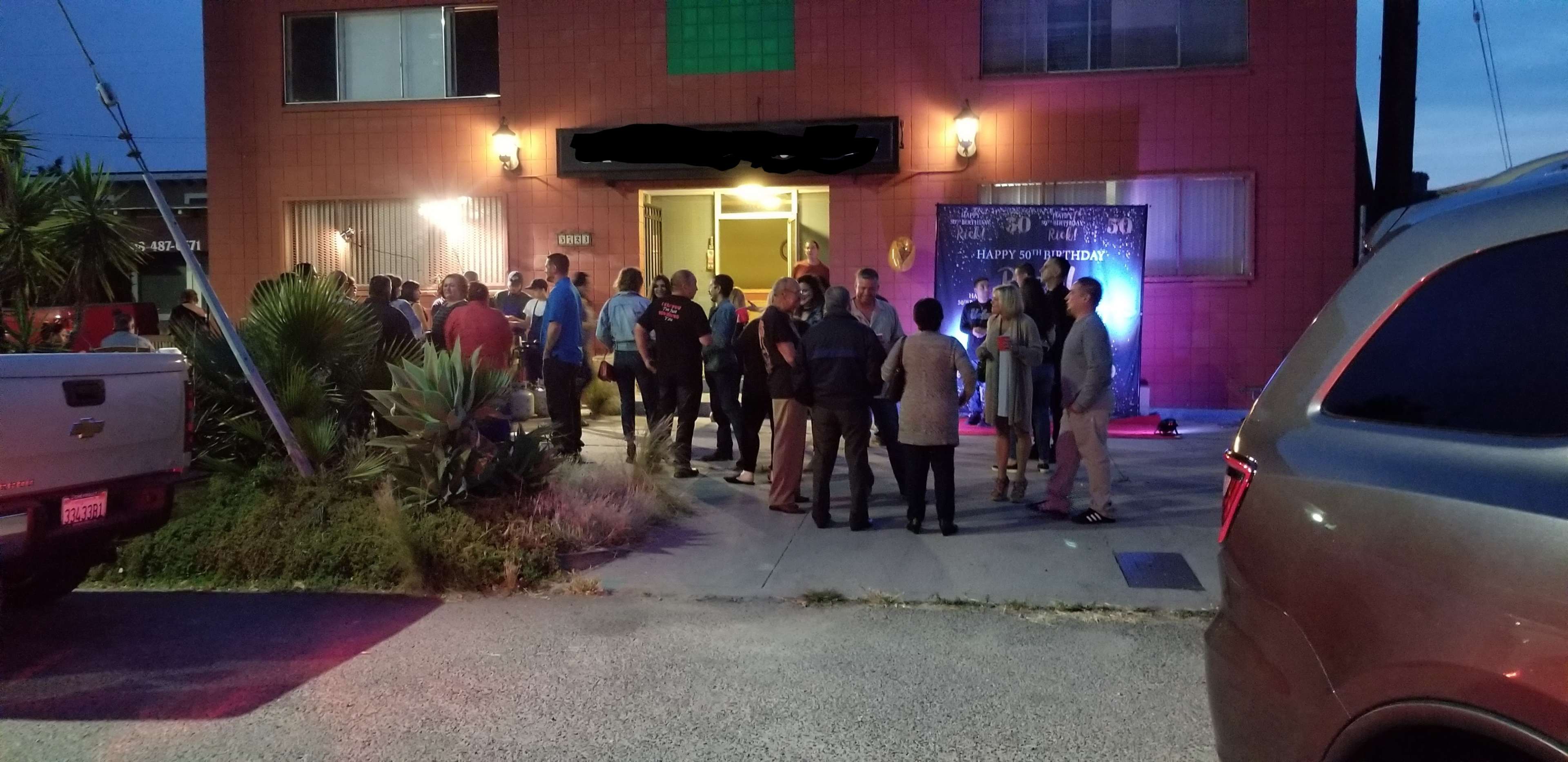 A group of people is gathered outside an apartment building during twilight.