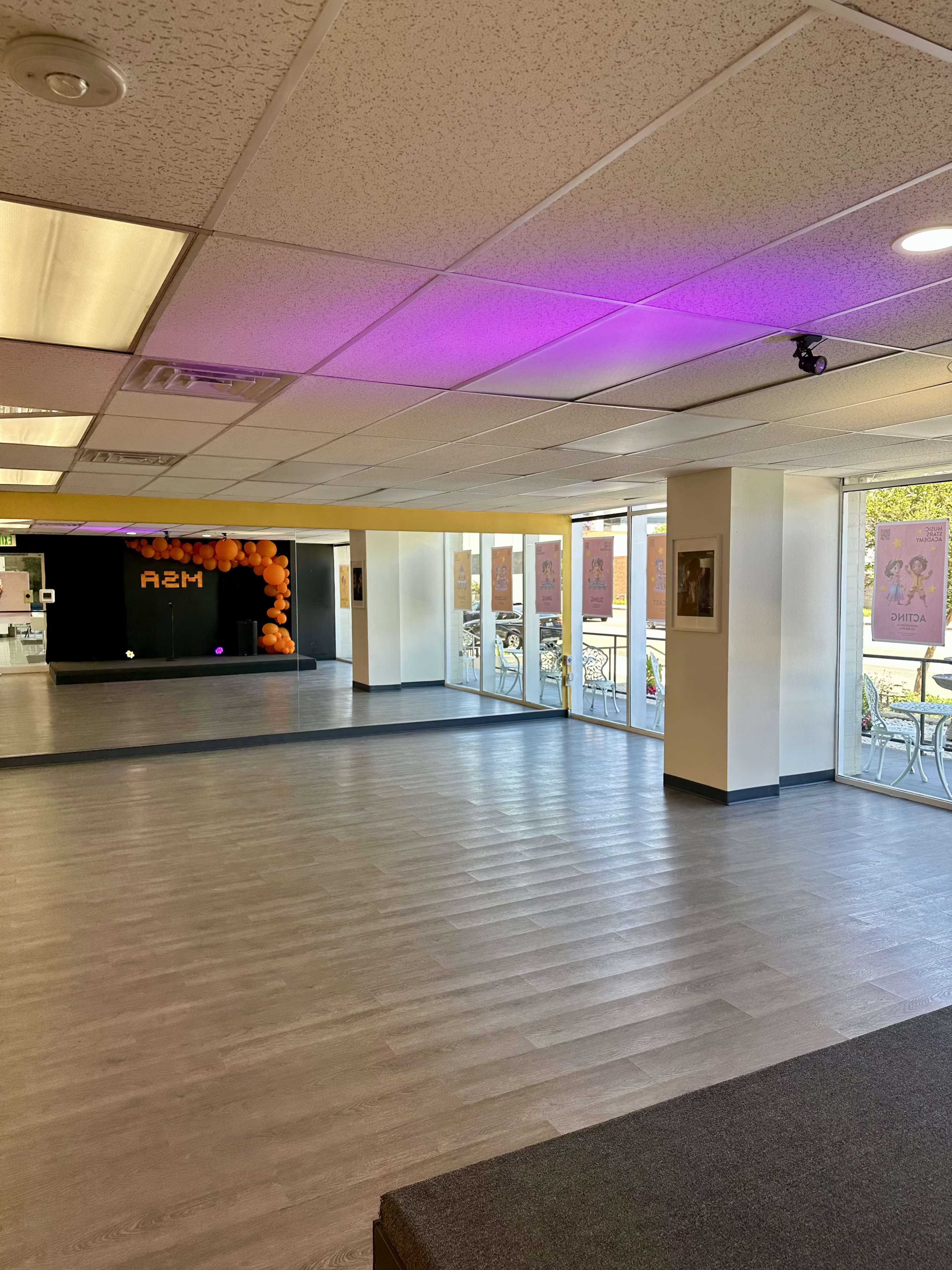 The image shows a spacious, well-lit studio with large windows, a mirrored wall, and orange balloons at one corner.