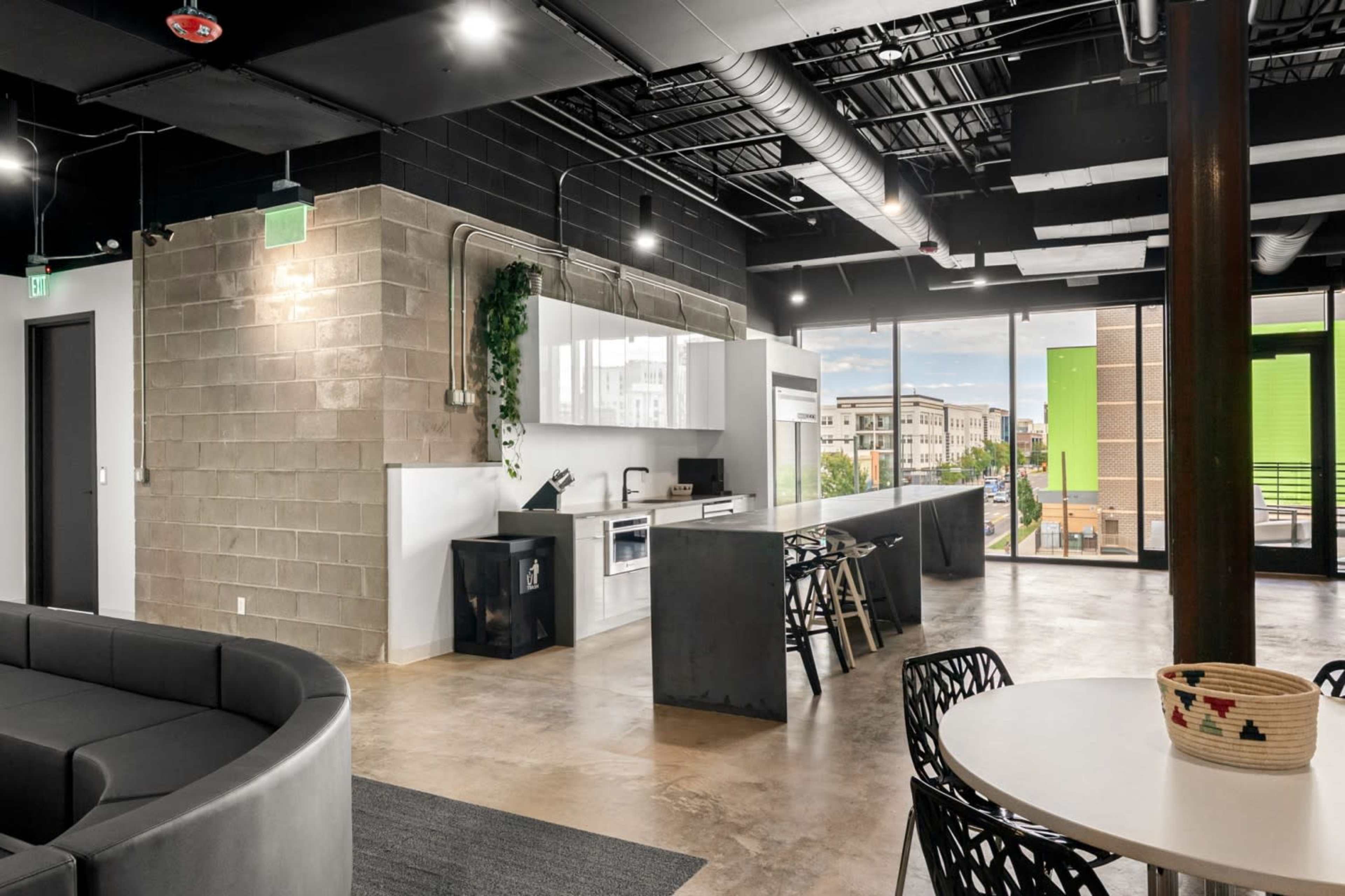The image shows a modern open-concept kitchen and lounge area with seating, large windows, and industrial design elements.