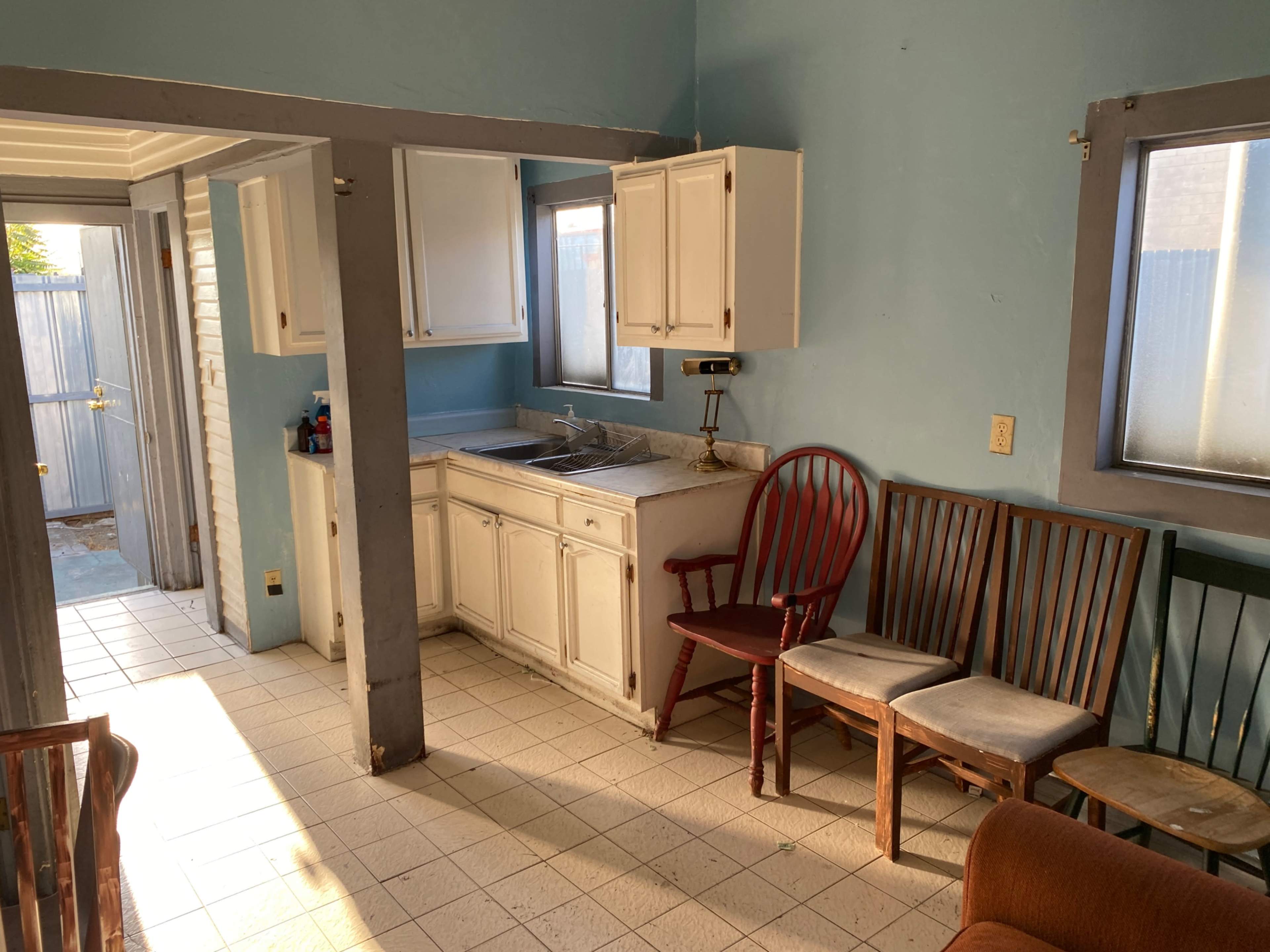 A small kitchen area features white cabinets, a sink, and several chairs arranged nearby.
