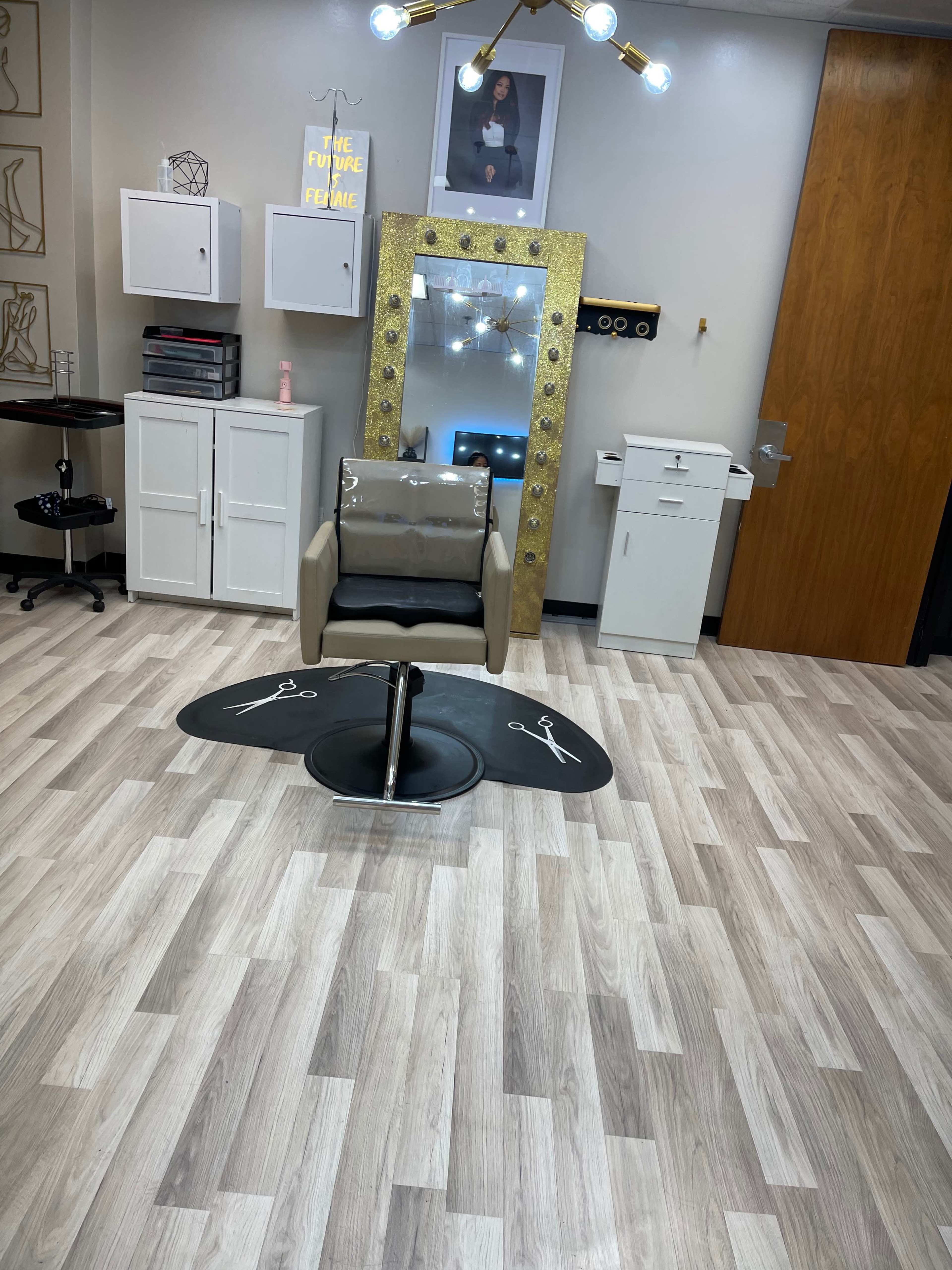 The image shows a salon or spa interior featuring a stylish chair, a large mirror with decorative lighting, and various cabinets and equipment on the walls.