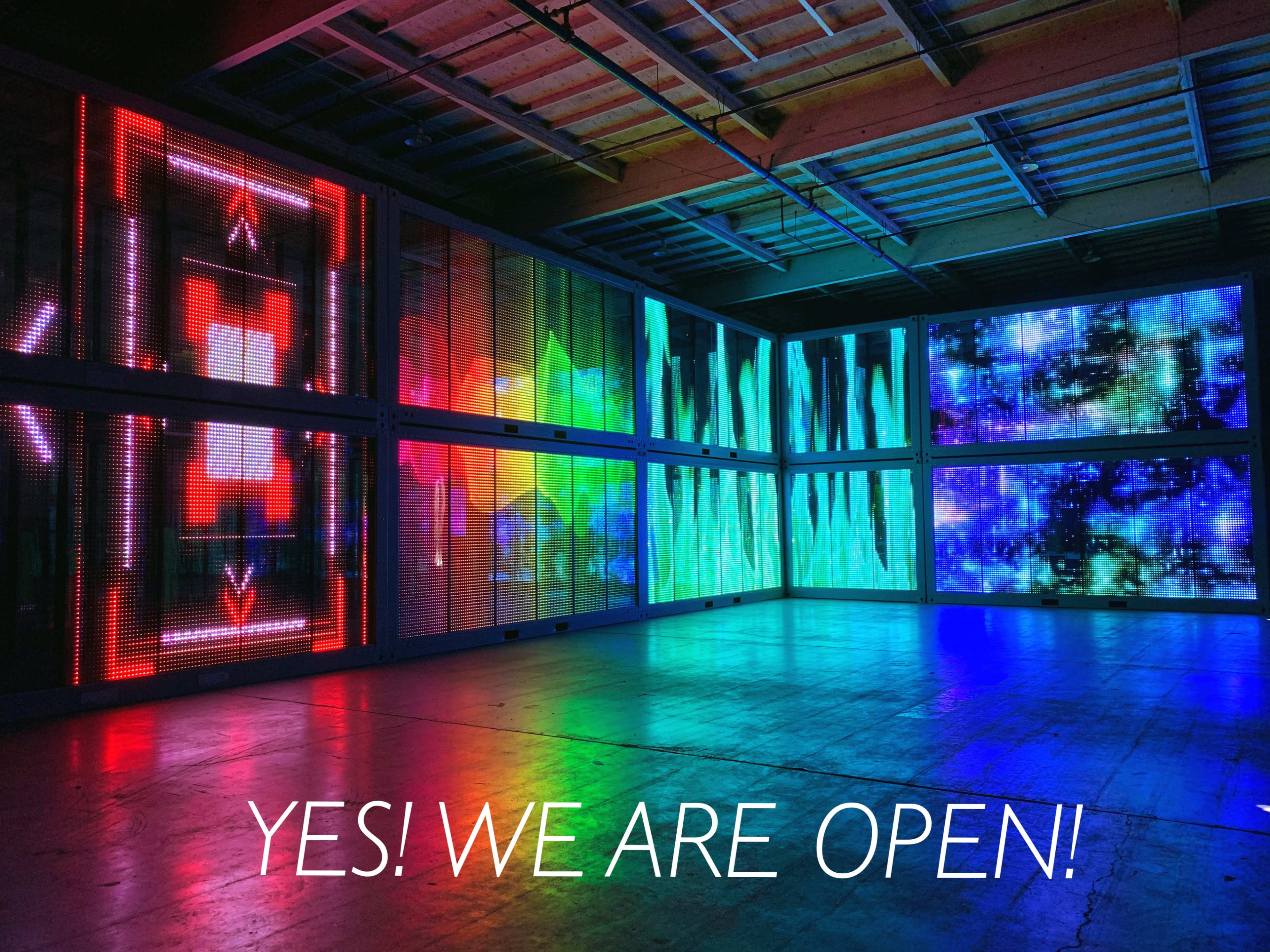 A colorful, illuminated art installation in a spacious room with a sign stating, "YES! WE ARE OPEN!"