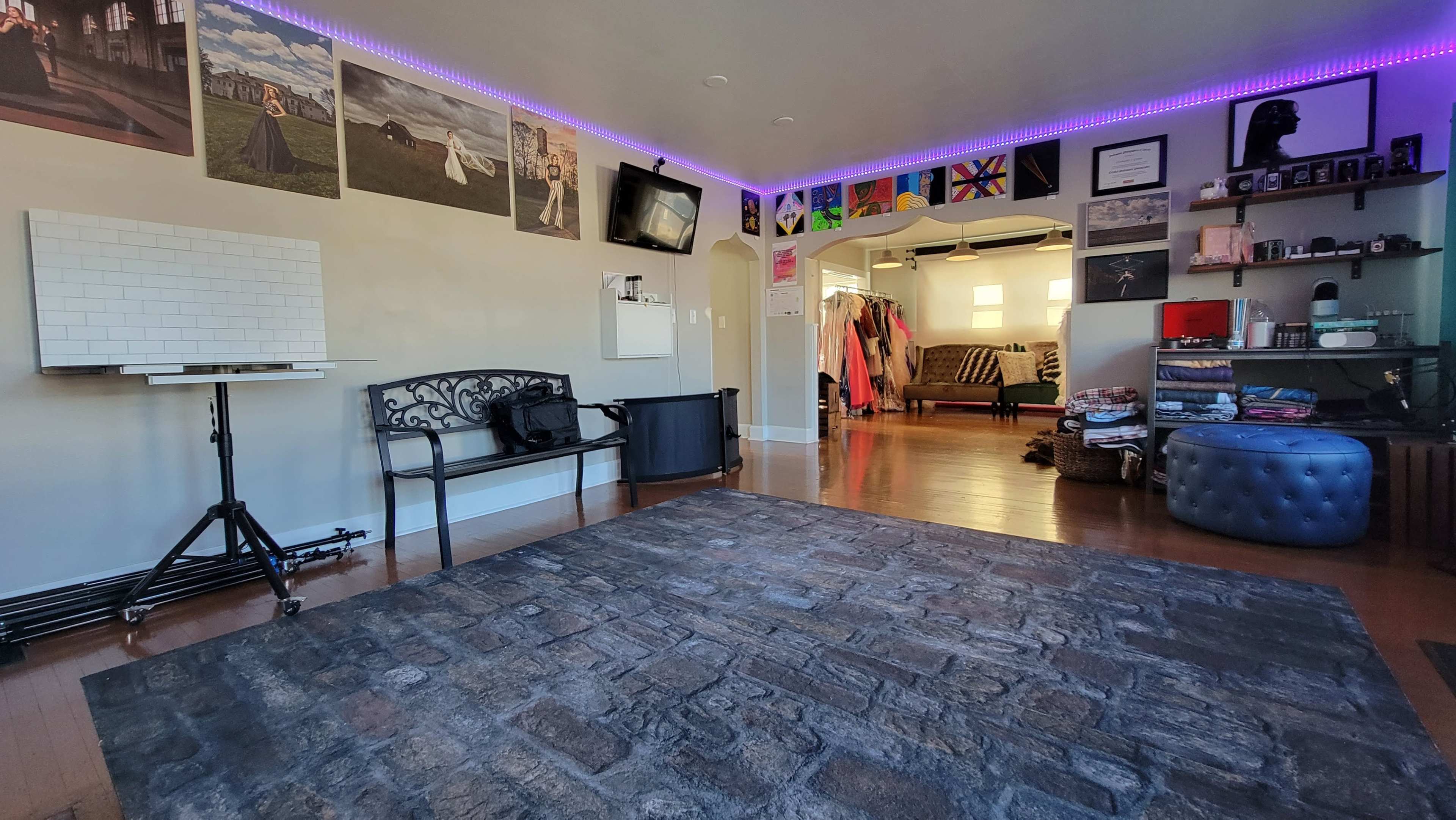A spacious room with a stone-patterned floor, a black bench, various artworks on the walls, and an open doorway leading to another area with clothing racks.