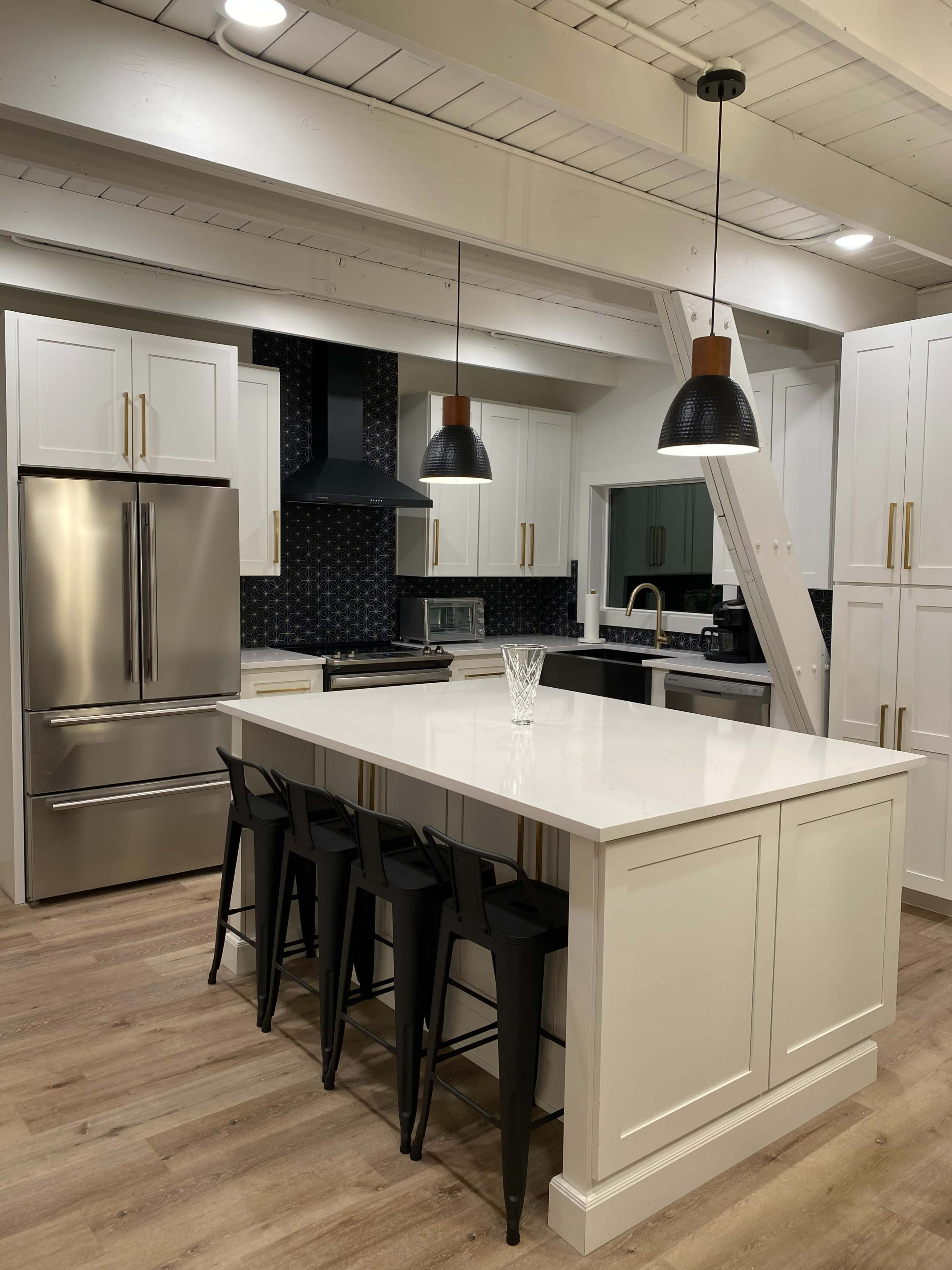 A modern kitchen features white cabinetry, a large island with black stools, and sleek metallic appliances.