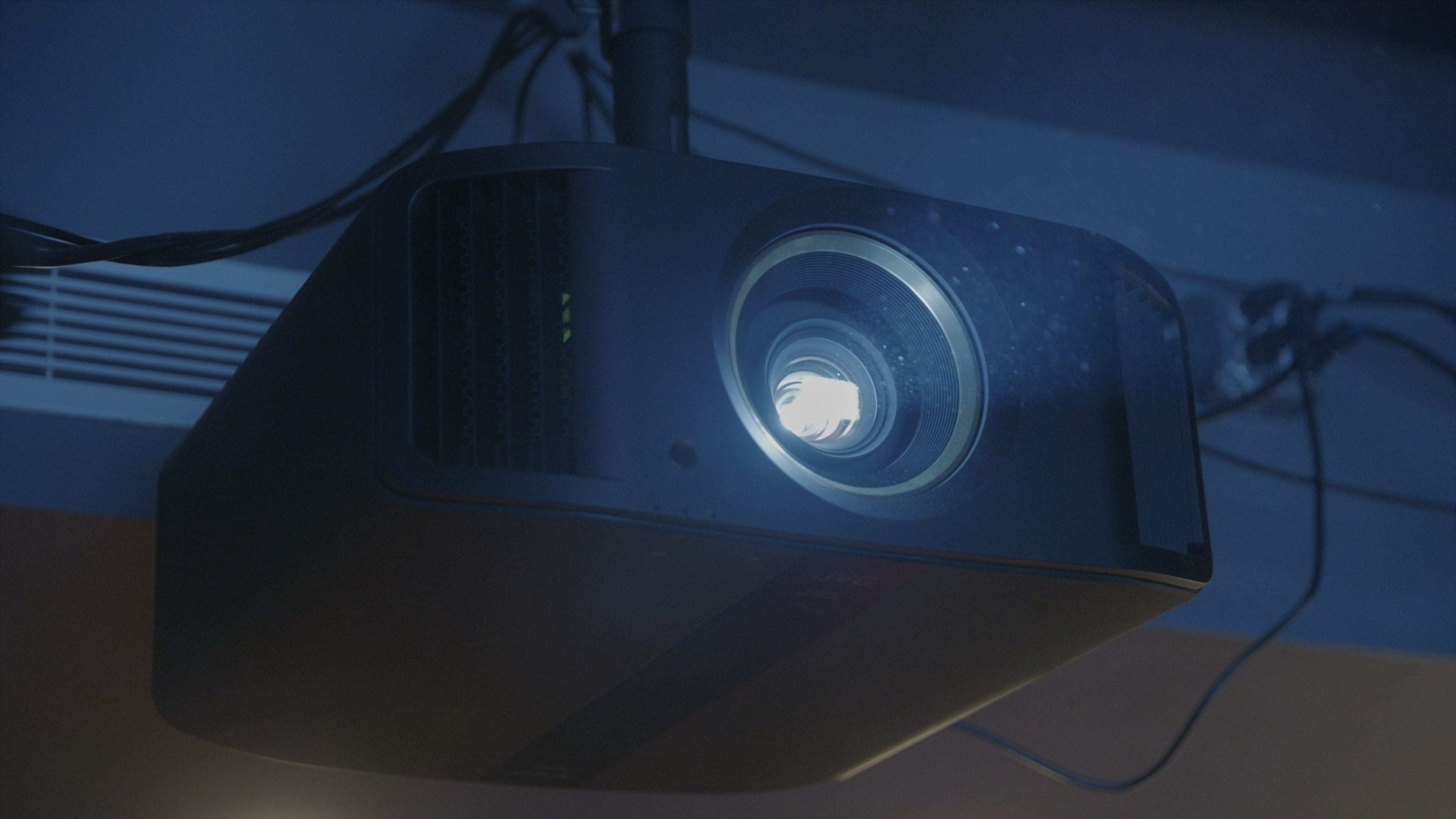 A ceiling-mounted projector emits light from its lens in a darkened room.