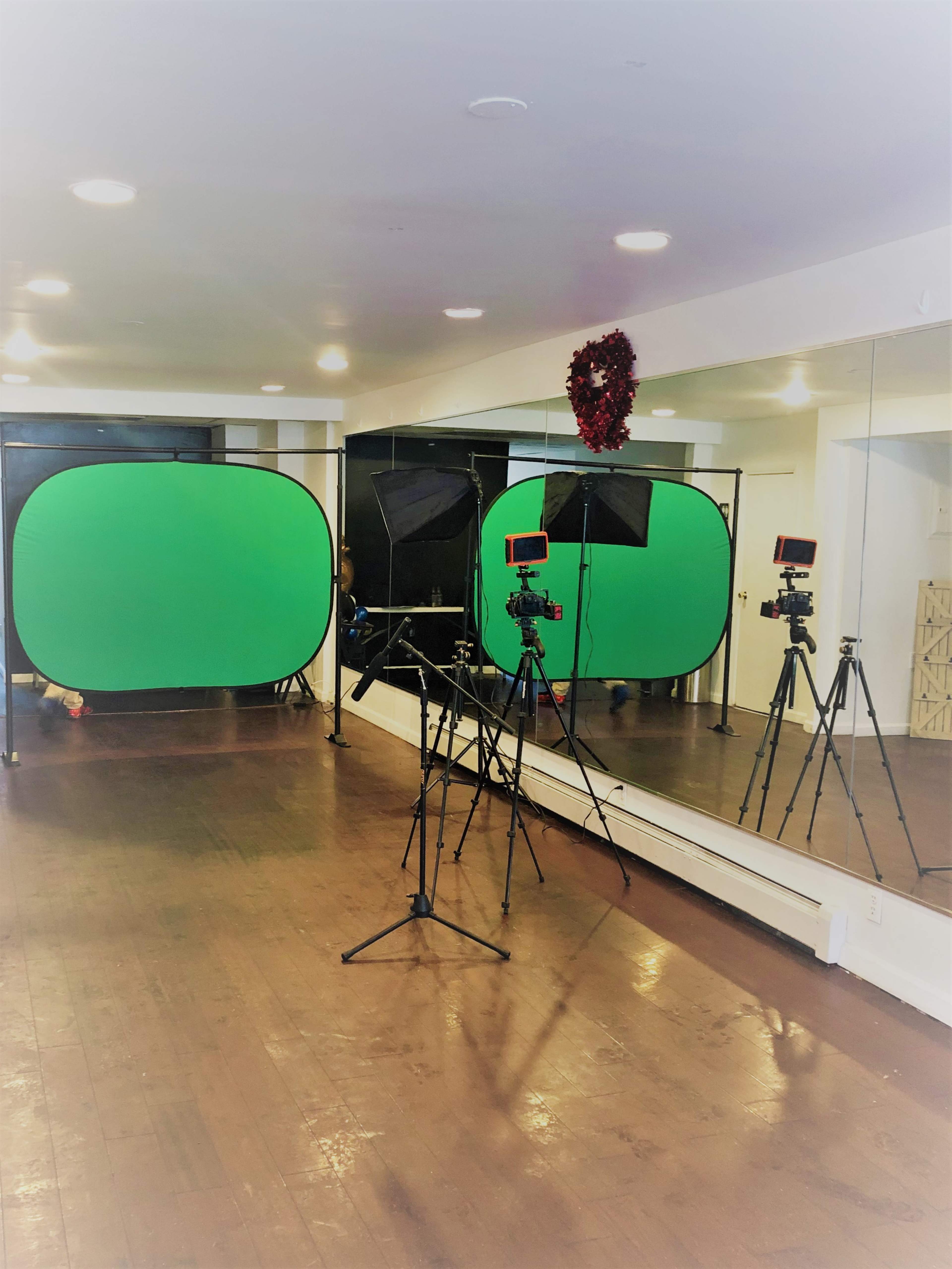 A studio space with green screen backdrops, tripods, and lighting equipment set up in front of a mirror.