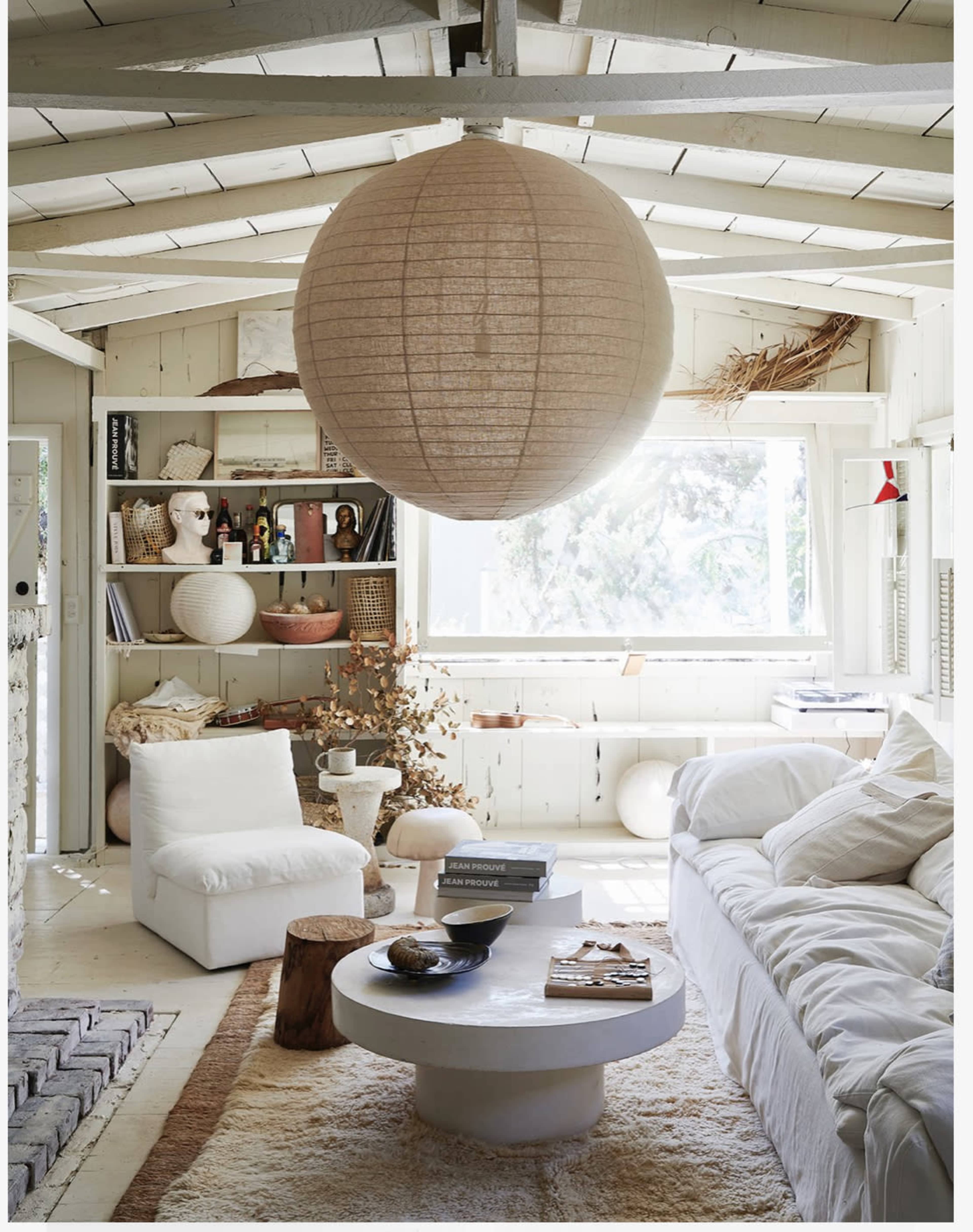 A spacious living room features a large paper lantern hanging overhead, with a white couch, circular coffee table, and shelves displaying various decor items.