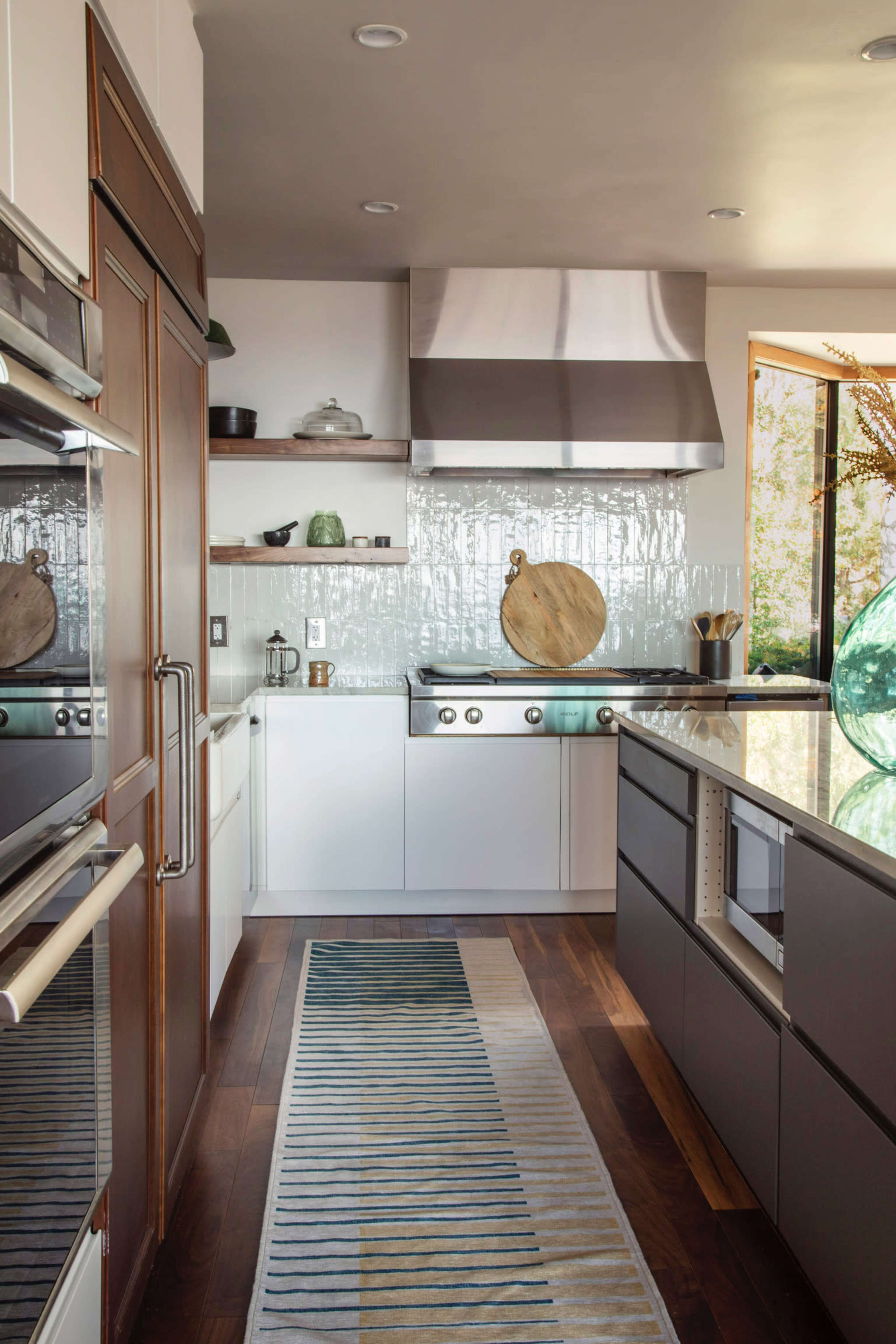 A modern kitchen features stainless steel appliances, a tiled backsplash, and a striped runner rug over hardwood flooring.