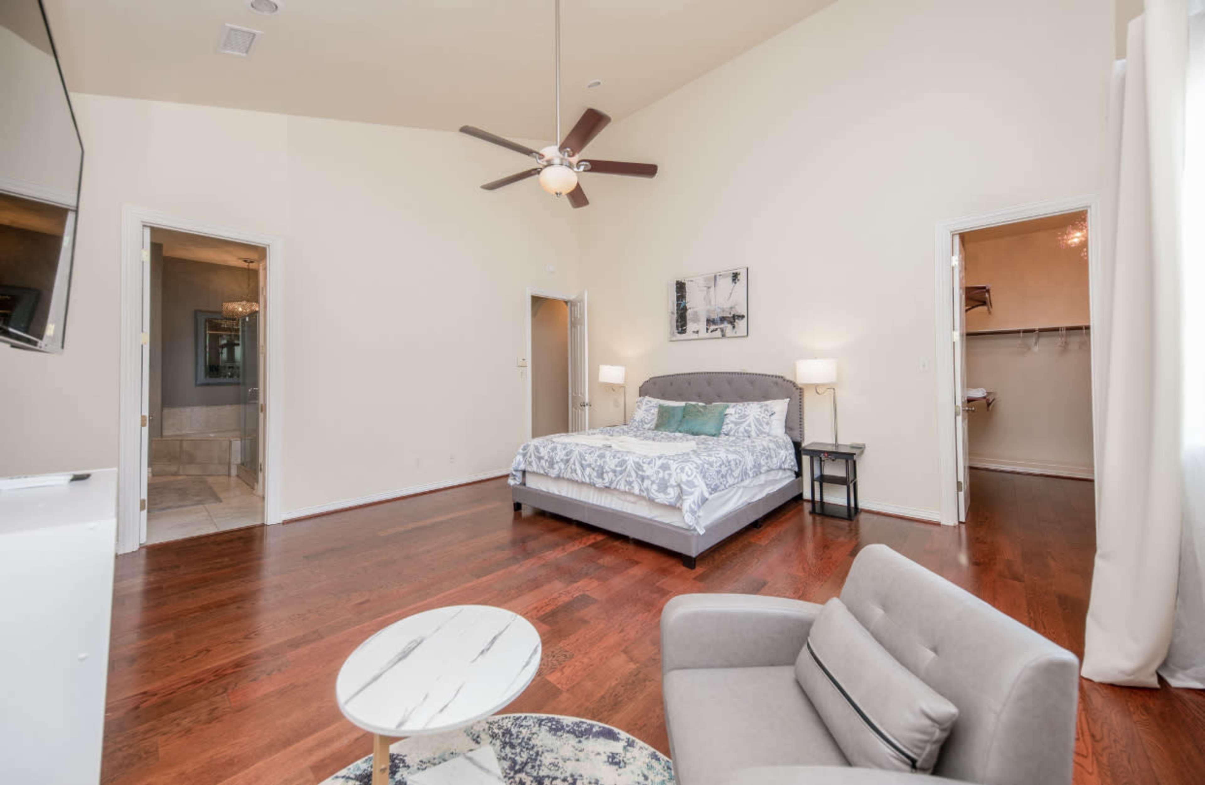 The image shows a spacious bedroom with a bed, a chair, a small table, and two doorways leading to adjacent areas.