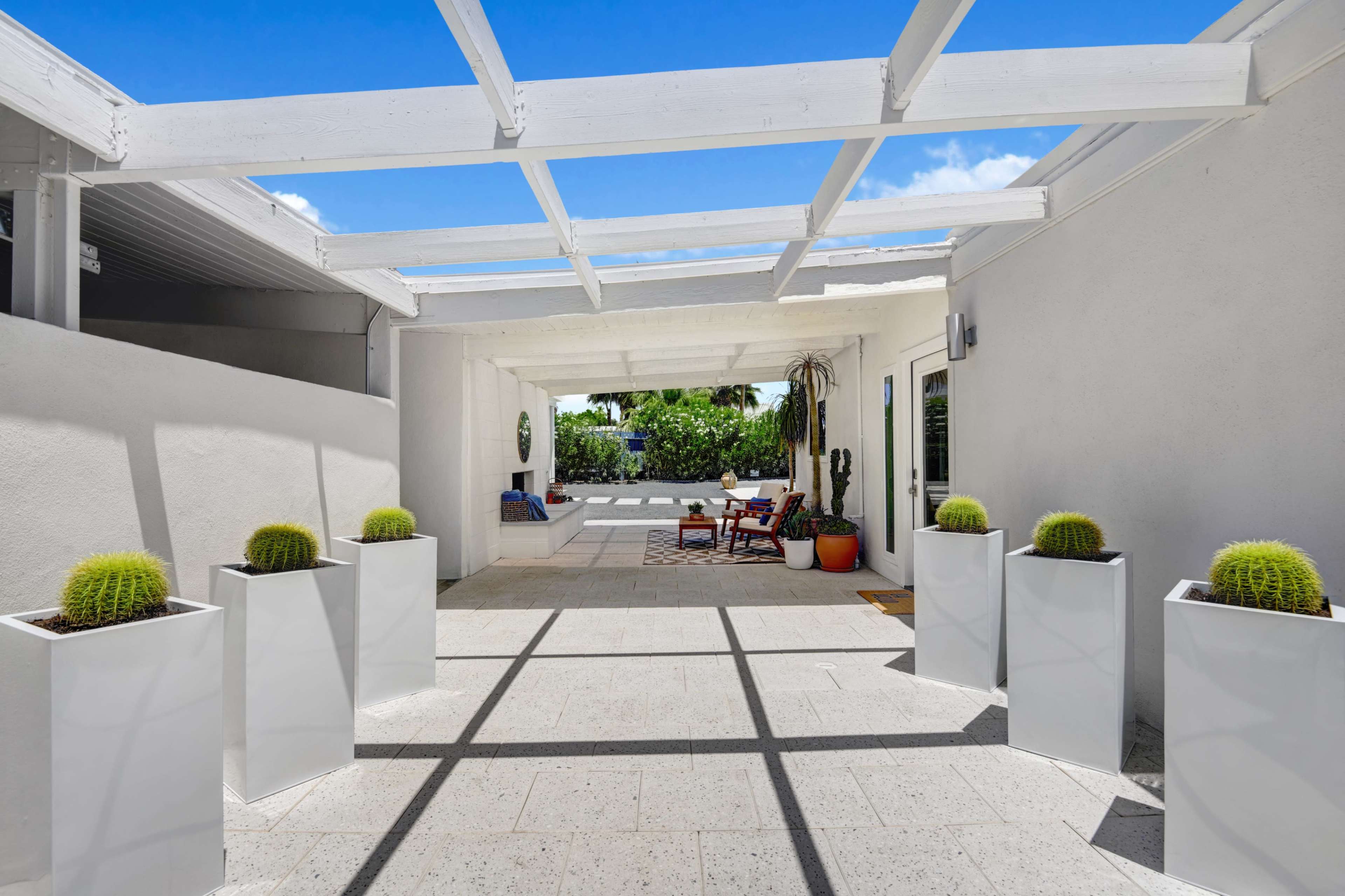 A modern outdoor courtyard features potted cacti in white planters, with a shaded seating area in the background.