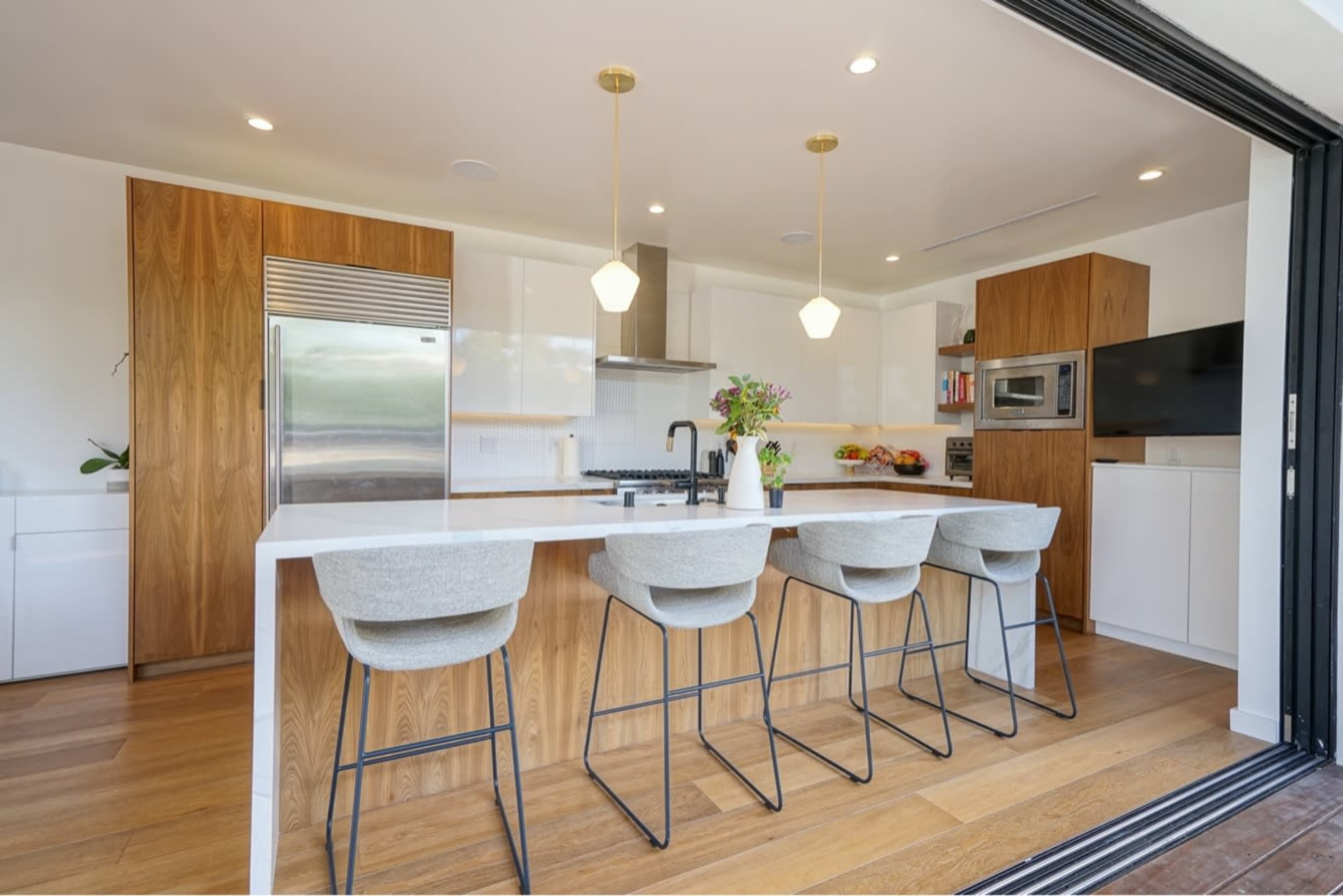 The image shows a modern kitchen with a large island, bar stools, and wooden cabinetry.