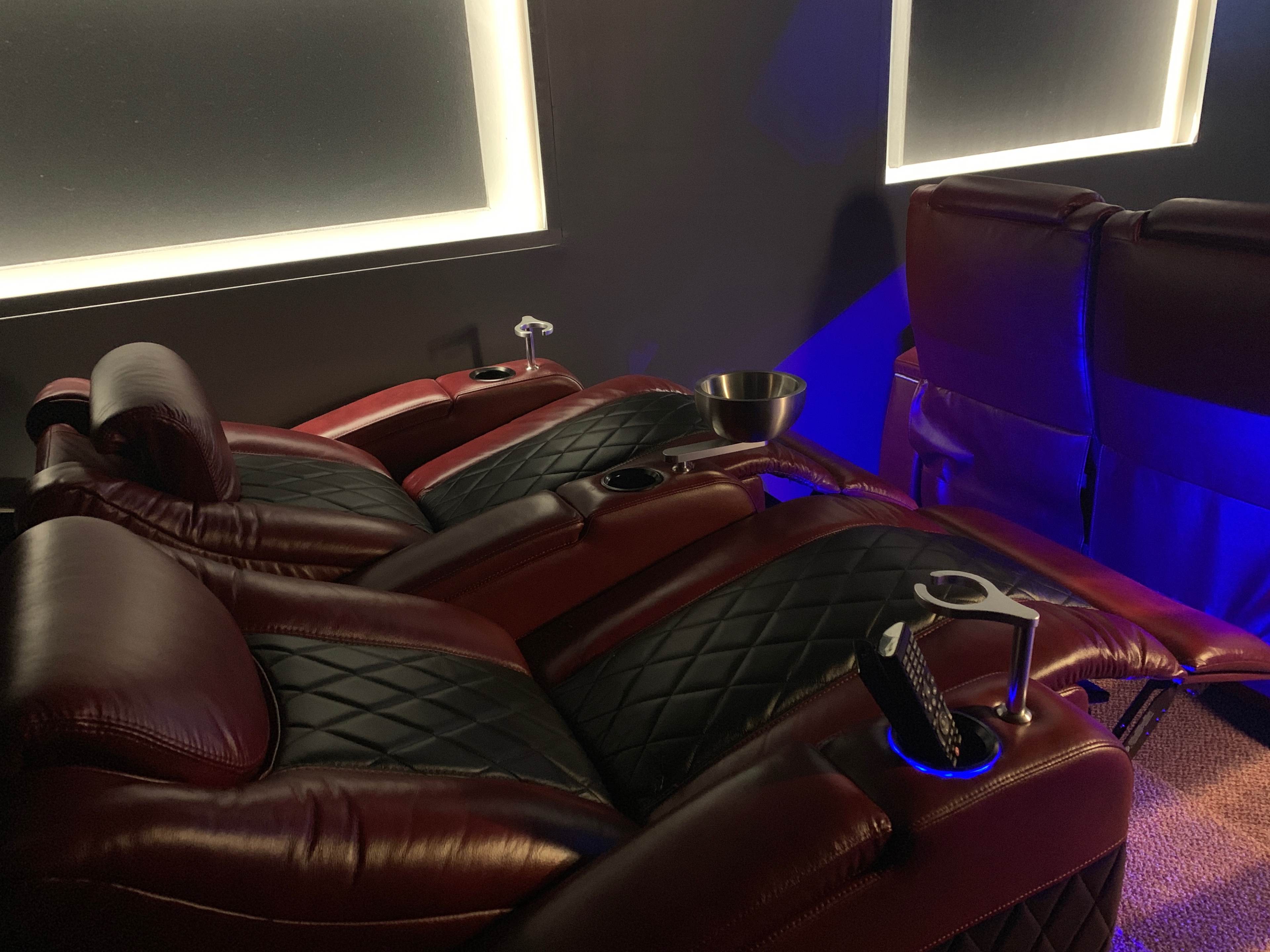 A pair of luxurious red leather recliners arranged in a cozy, dark setting, equipped with cup holders and a small bowl.