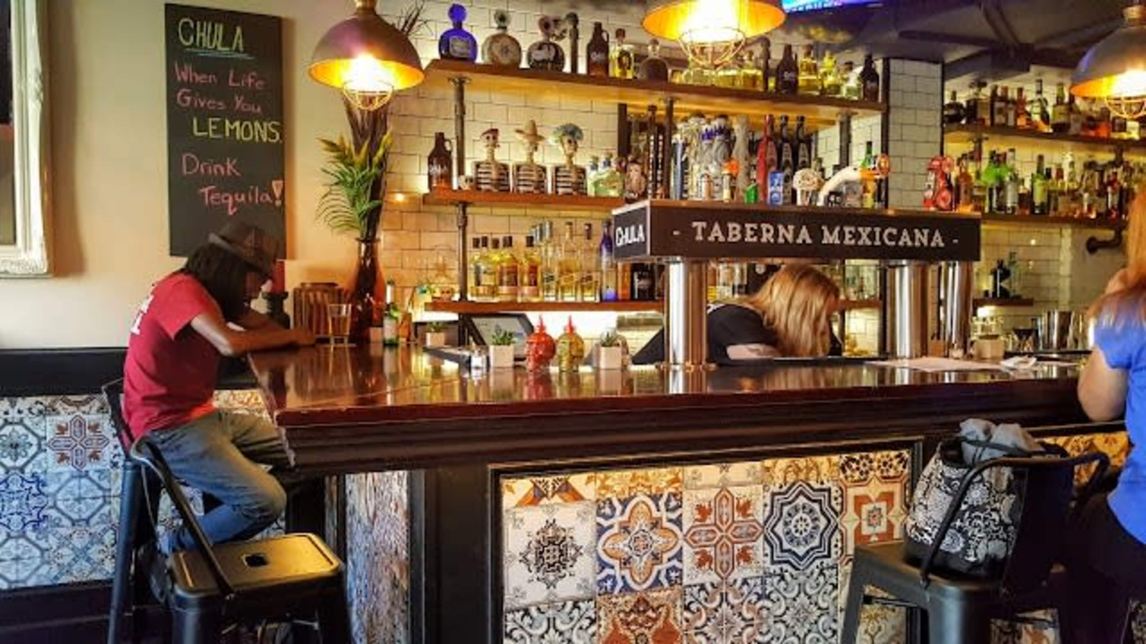 A man sits at the bar while two bartenders prepare drinks in a colorful Mexican restaurant.
