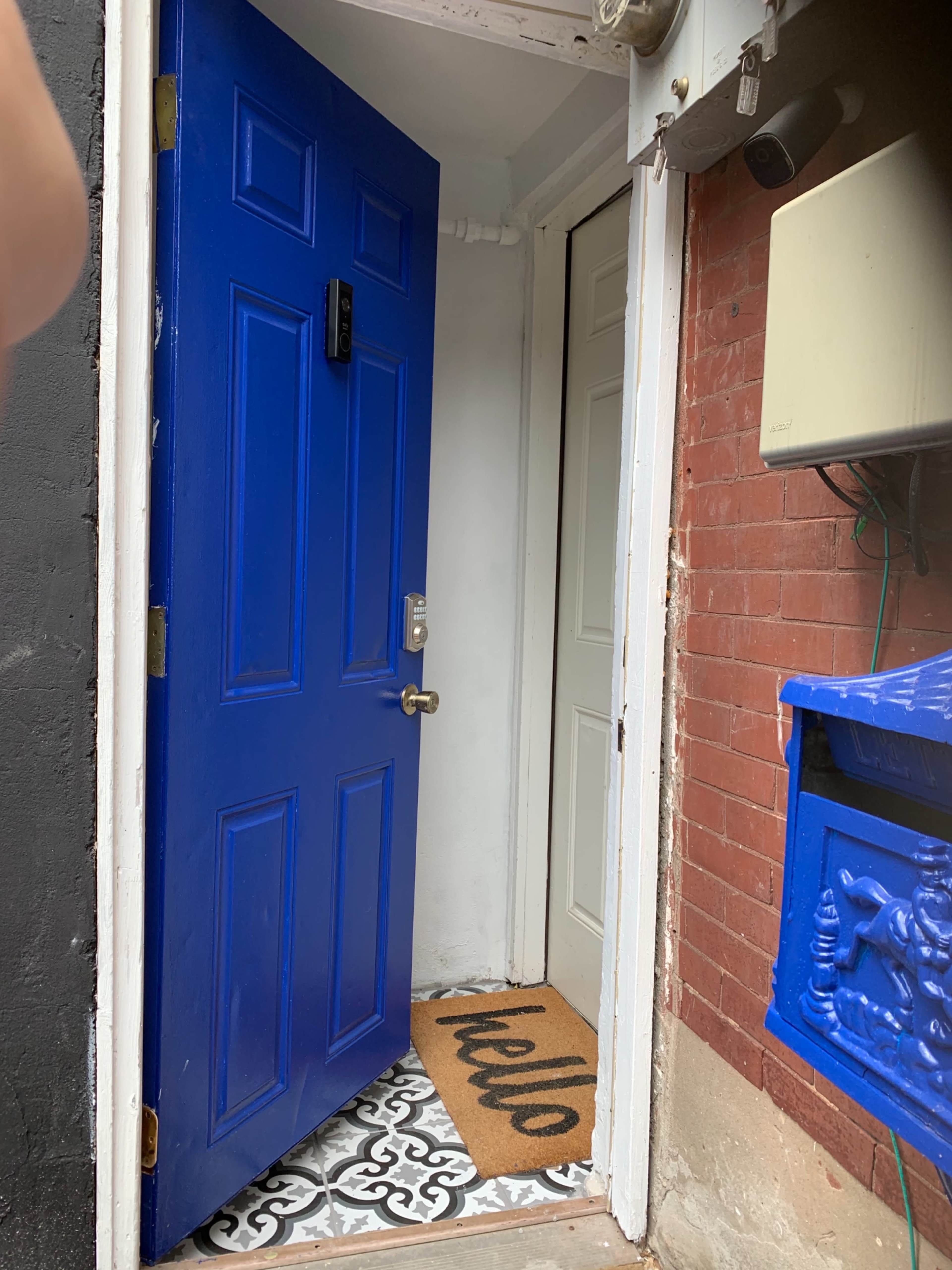 A blue door stands open to reveal a hallway with a decorative welcome mat and a closed white door nearby.