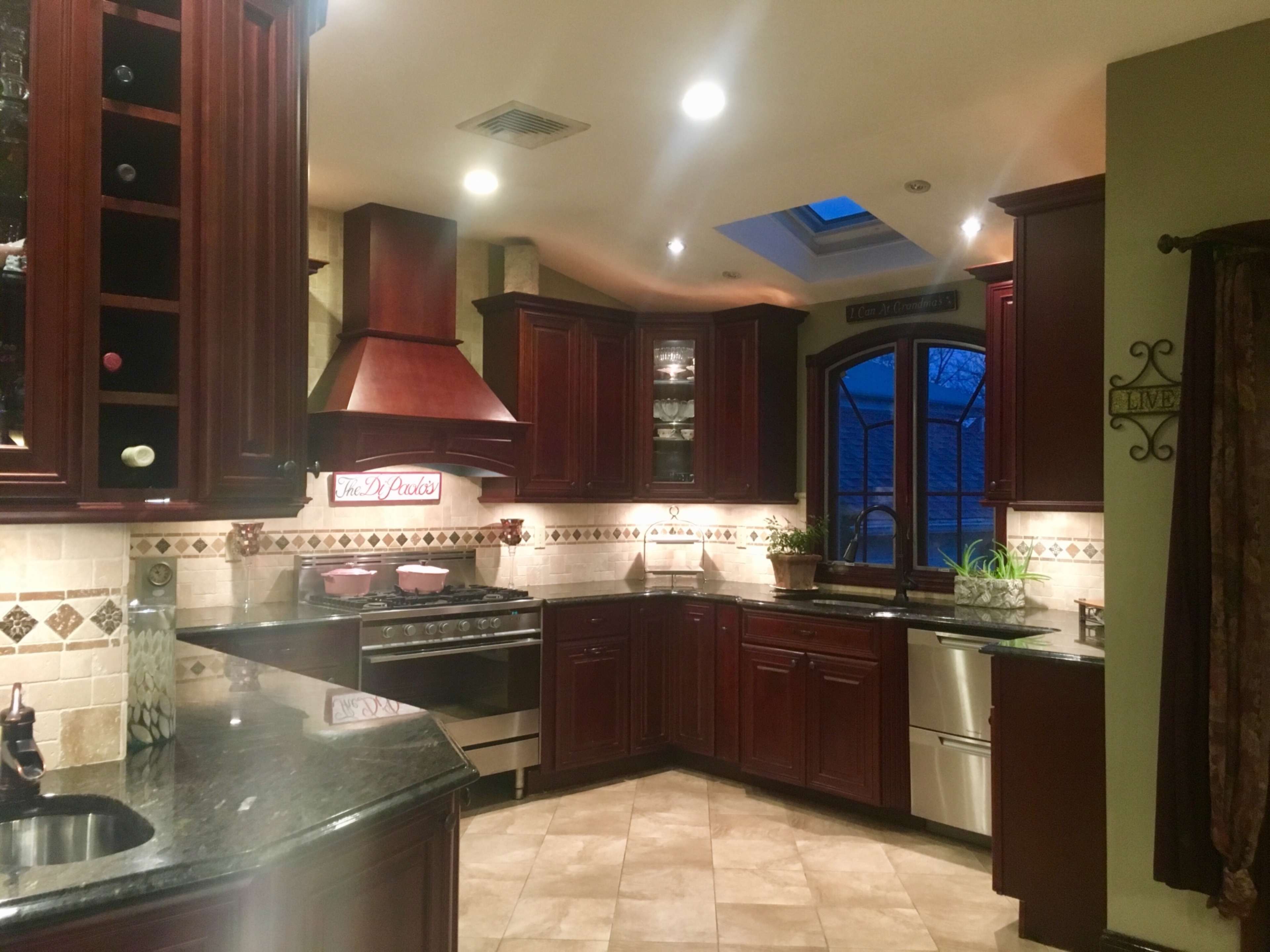 The kitchen features dark wooden cabinetry, a stainless steel stove, and a large window above the sink allowing natural light to enter.
